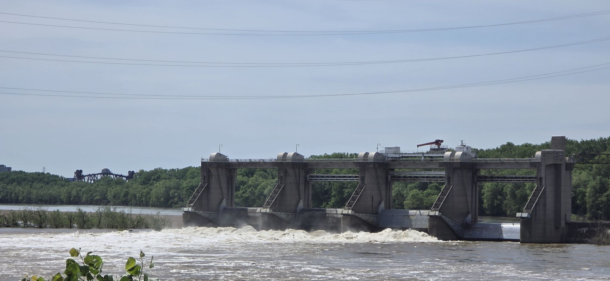 Concrete dam with rushing water, power lines overhead, and distant trees. - Lewis & Clark Cabins loop from Indiana University Southeast