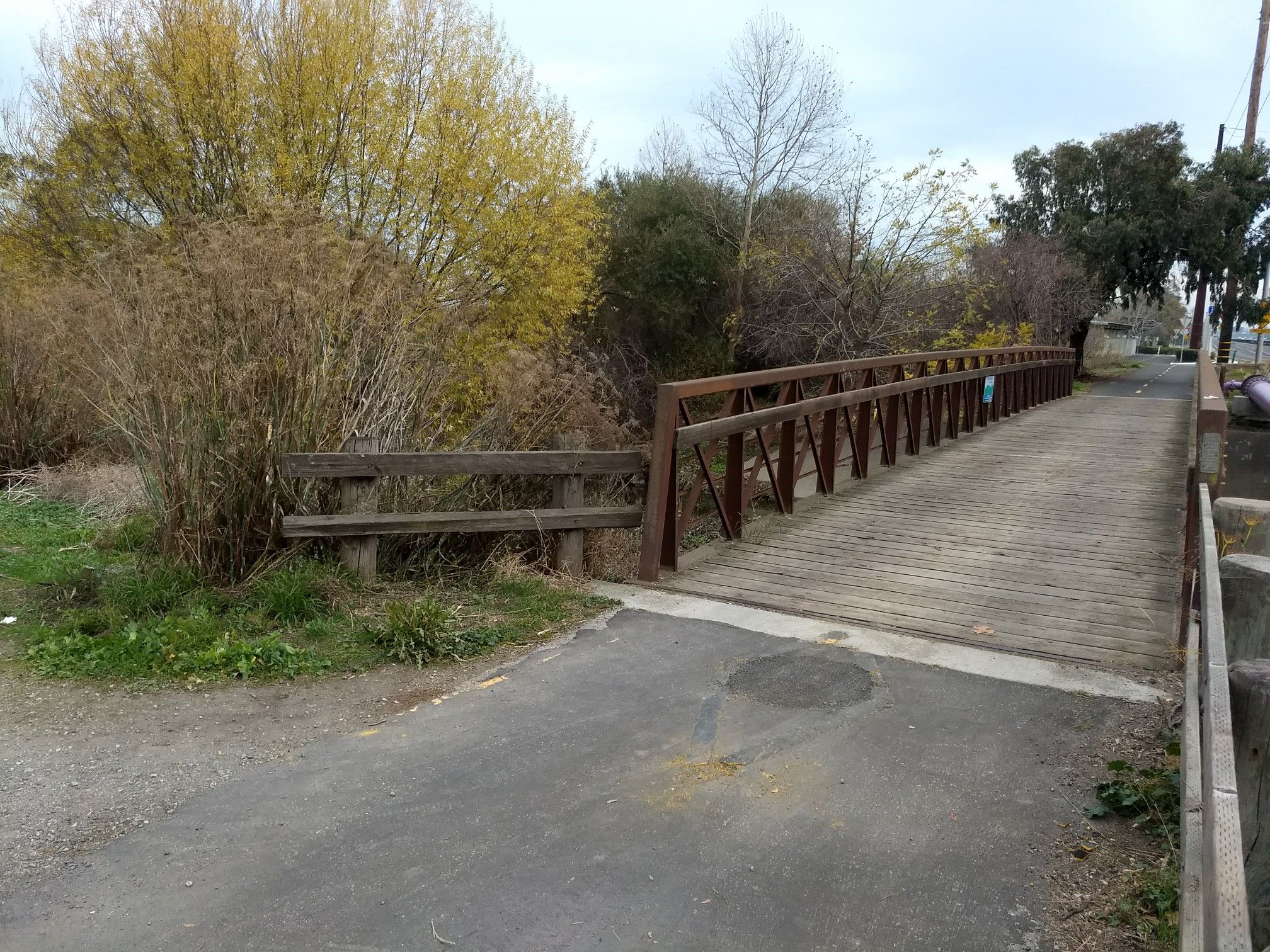 Wooden bridge over water, next to a paved path and autumn trees. - Adobe Creek Trail: Byxbee Park to Freshwater Marsh at Matadero Creek
