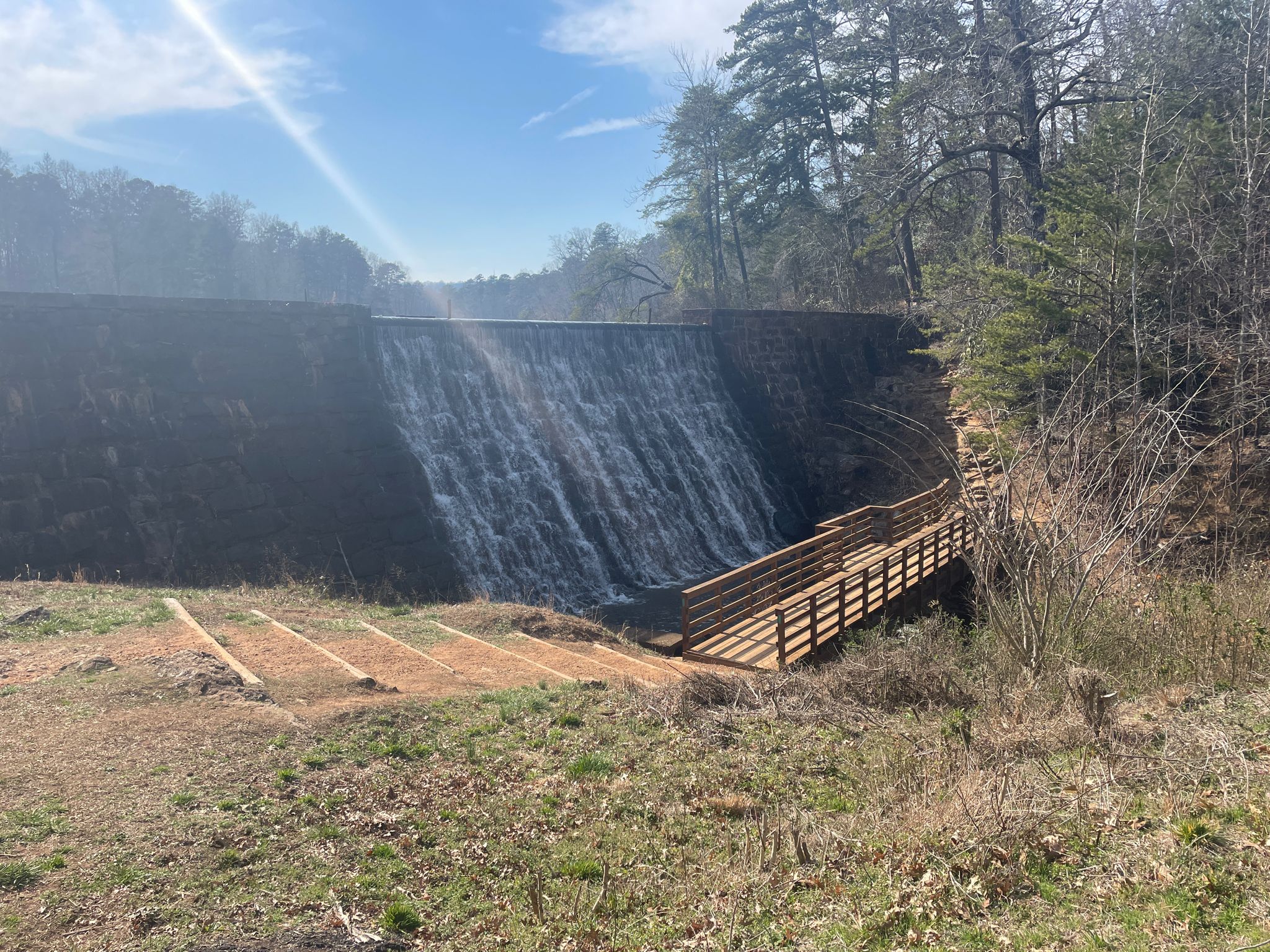 A dam with water cascading down, next to a wooden walkway. - Back-side of Paris Mountain State Park loop