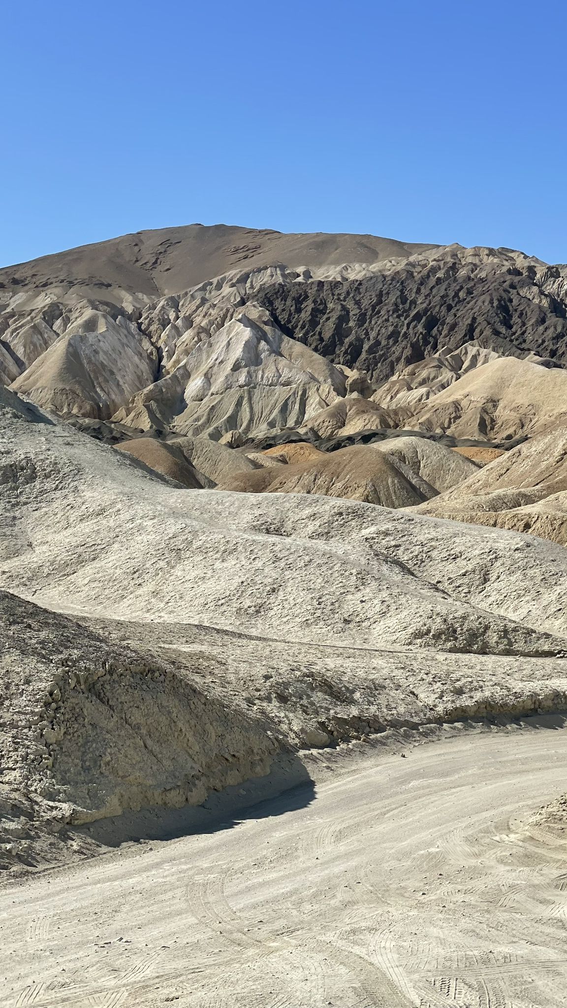 Winding dirt road through colorful, arid desert mountains under a clear blue sky. - Twenty Mule Team Canyon