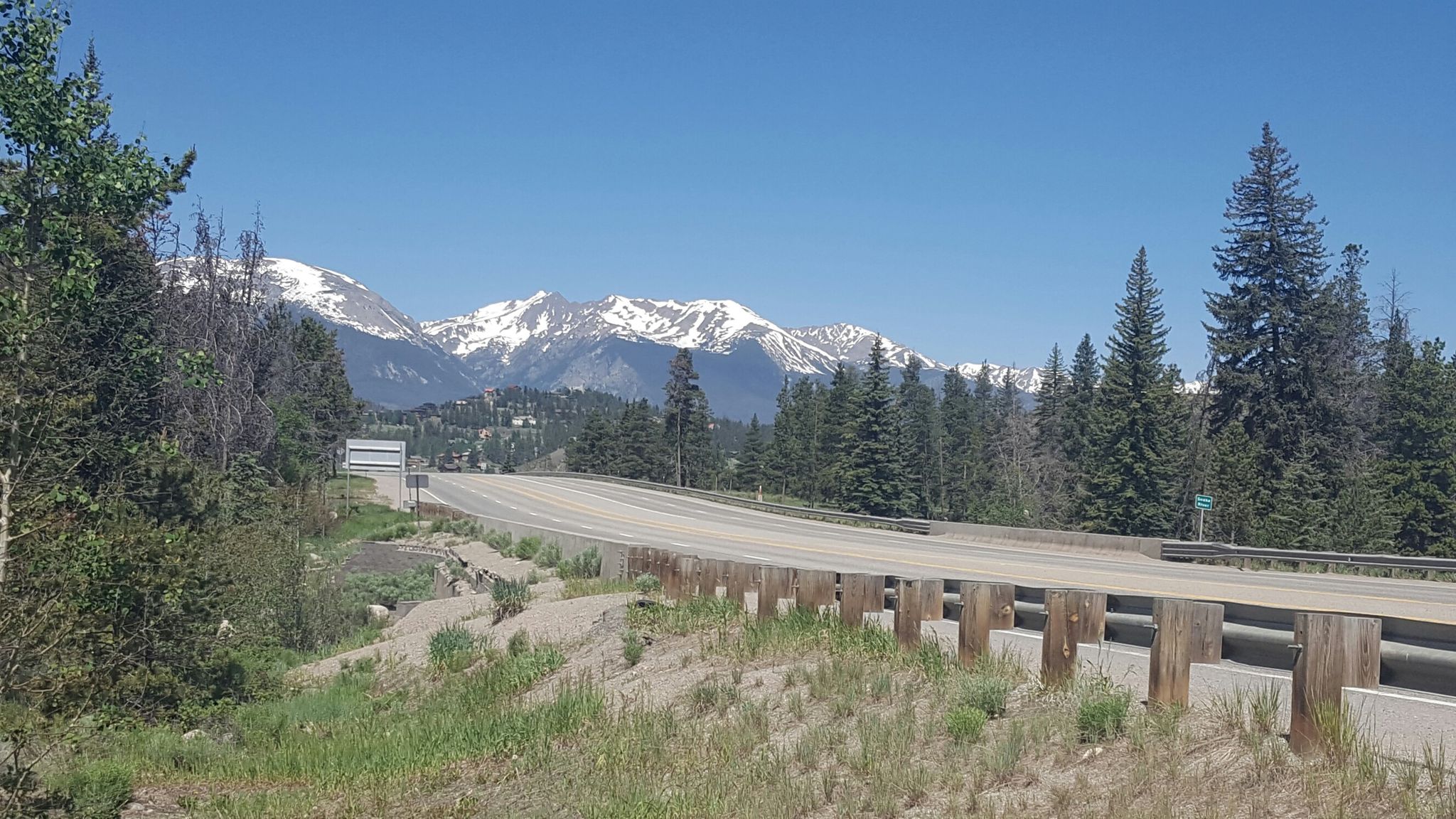 A highway bridge surrounded by pine trees, with snow-capped mountains under blue sky. - Snake River Trail – Snake River Trail loop from Flying Dutchman
