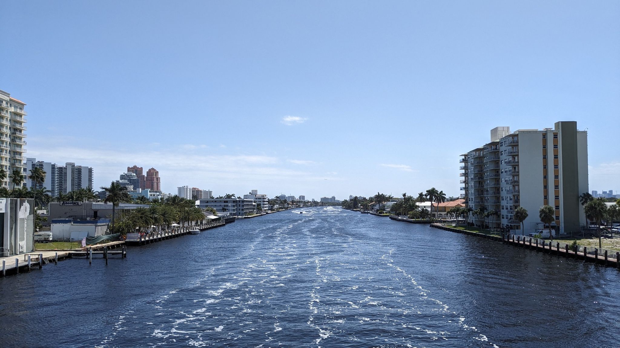 A wide canal with boat wakes, flanked by city buildings under a clear sky. - Lauderdale-by-the-Sea Beach loop