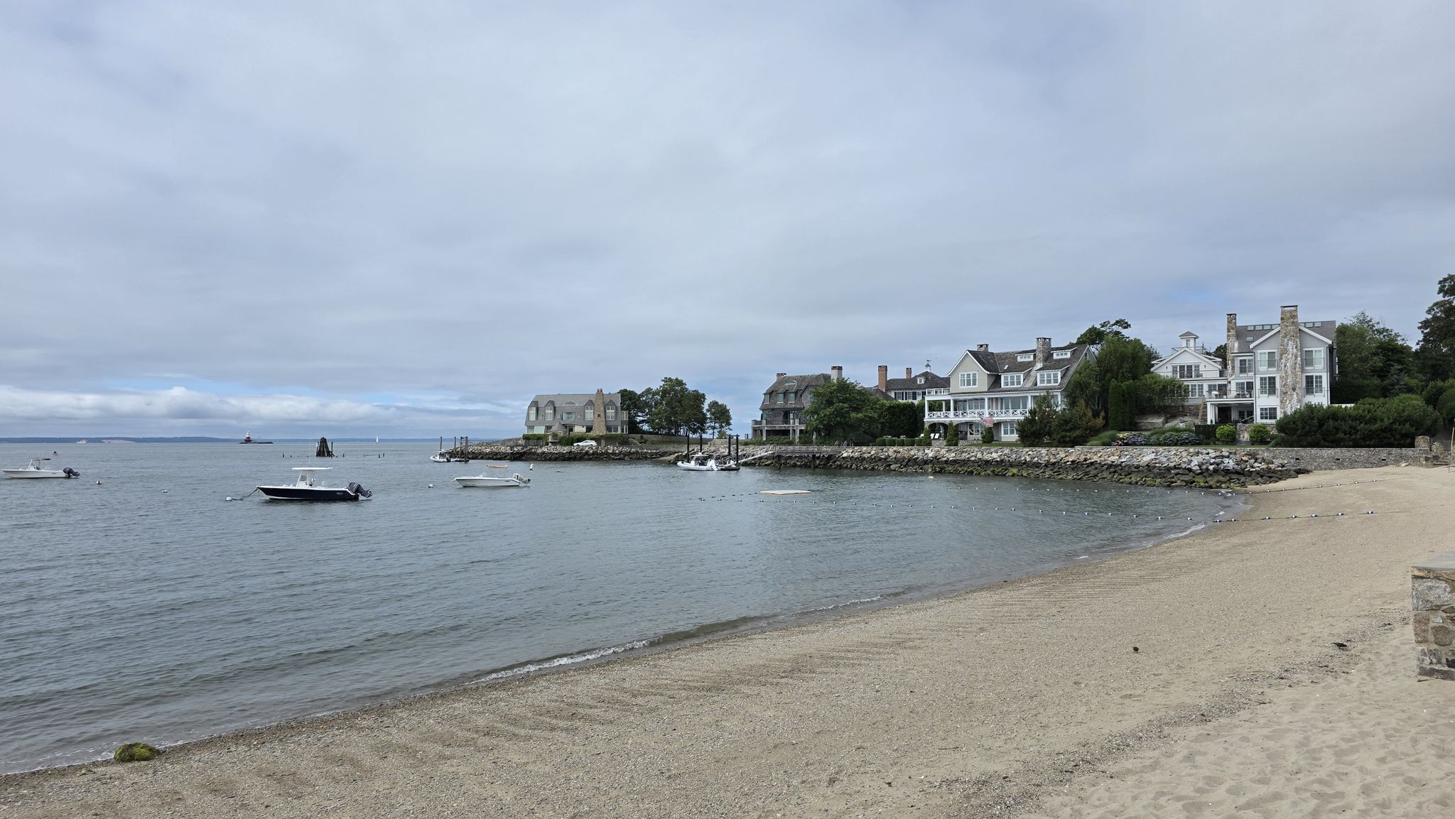 Sandy beach and calm water with houses under an overcast sky. - Crescent Beach loop from Rowayton