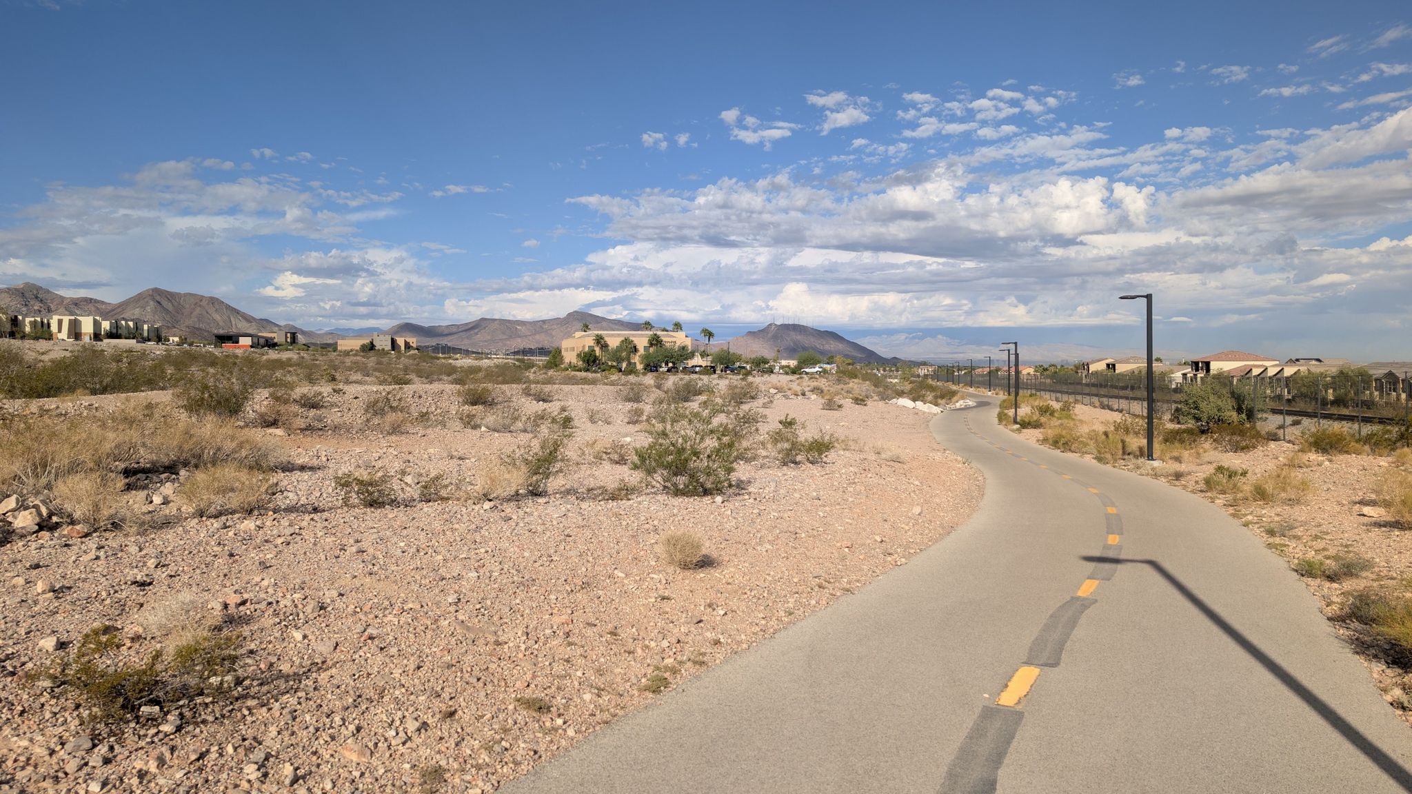 Winding paved path through arid landscape with distant mountains under blue sky. - Hiking loop from Nevada State College