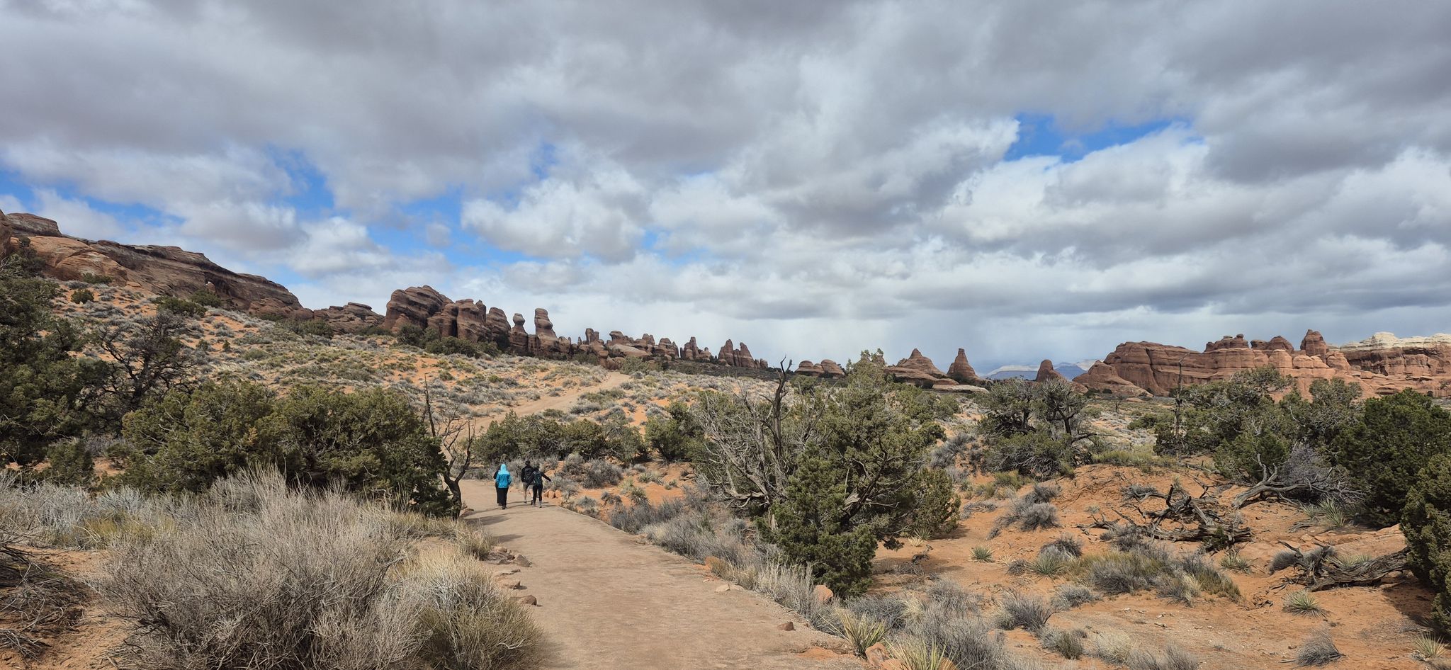 Two hikers on a dirt path through desert landscape under cloudy sky. - Devil's Garden Primitive Loop