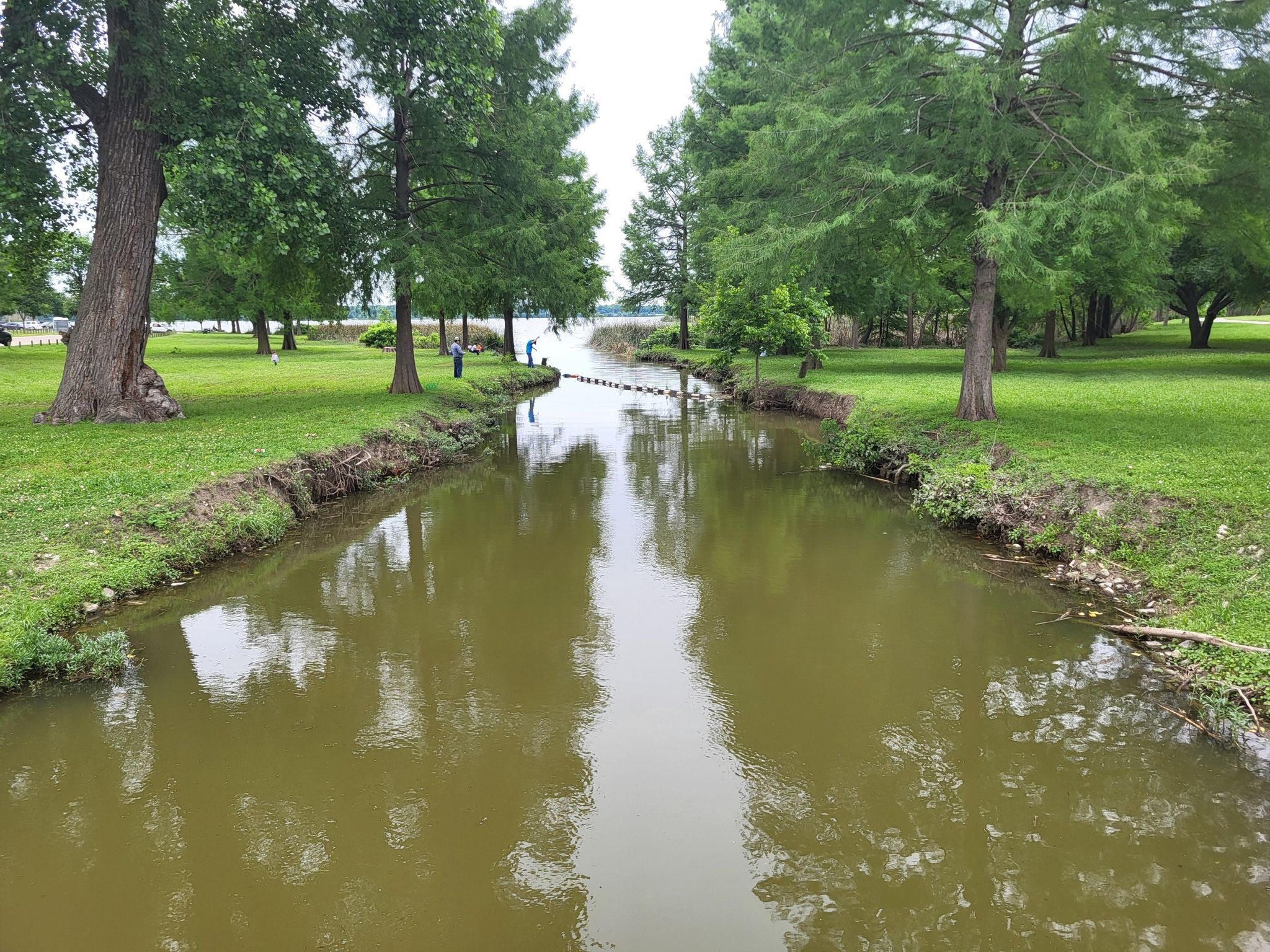 A narrow canal flows between grassy banks with distant trees and people. - SoPac Trail – White Rock Trail loop from Lovers Lane