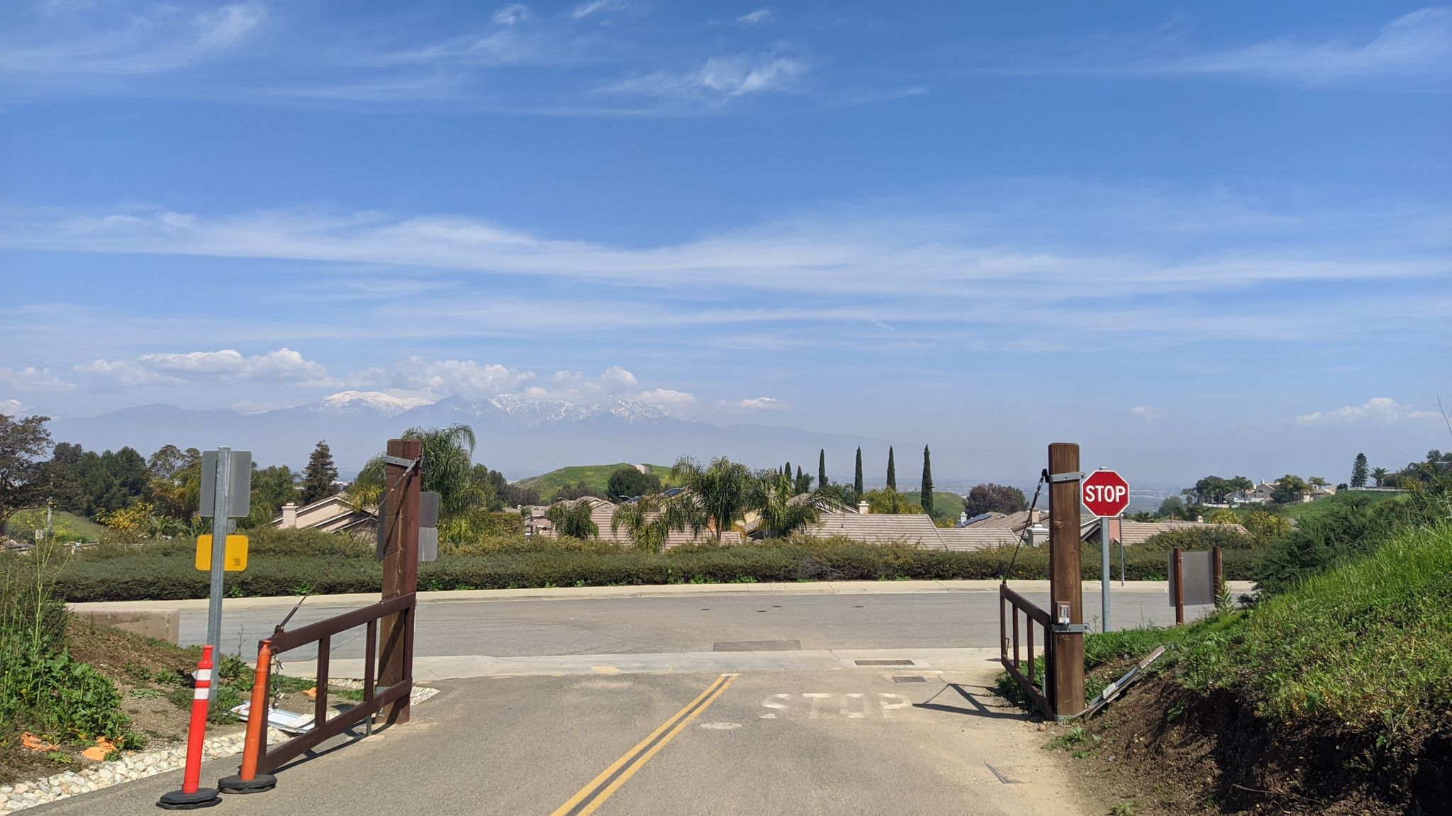 Gated road with a stop sign, houses in the sunny distance. - Telegraph Canyon Overlook