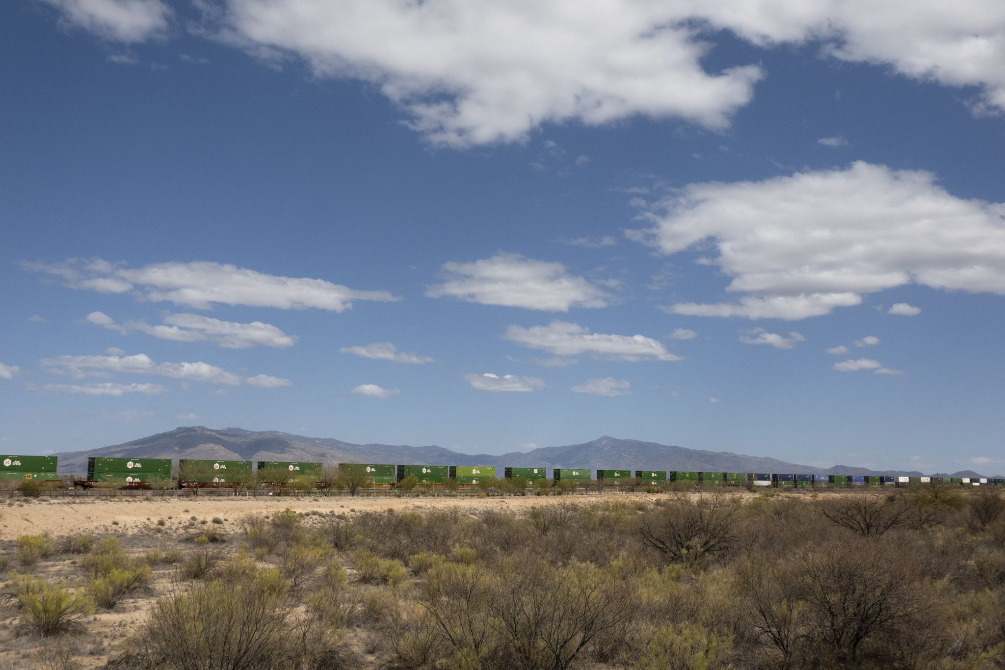 Long green train cars in a desert landscape with distant mountains. - Batty Biker – Pantano River Park loop from Trail Dust Town