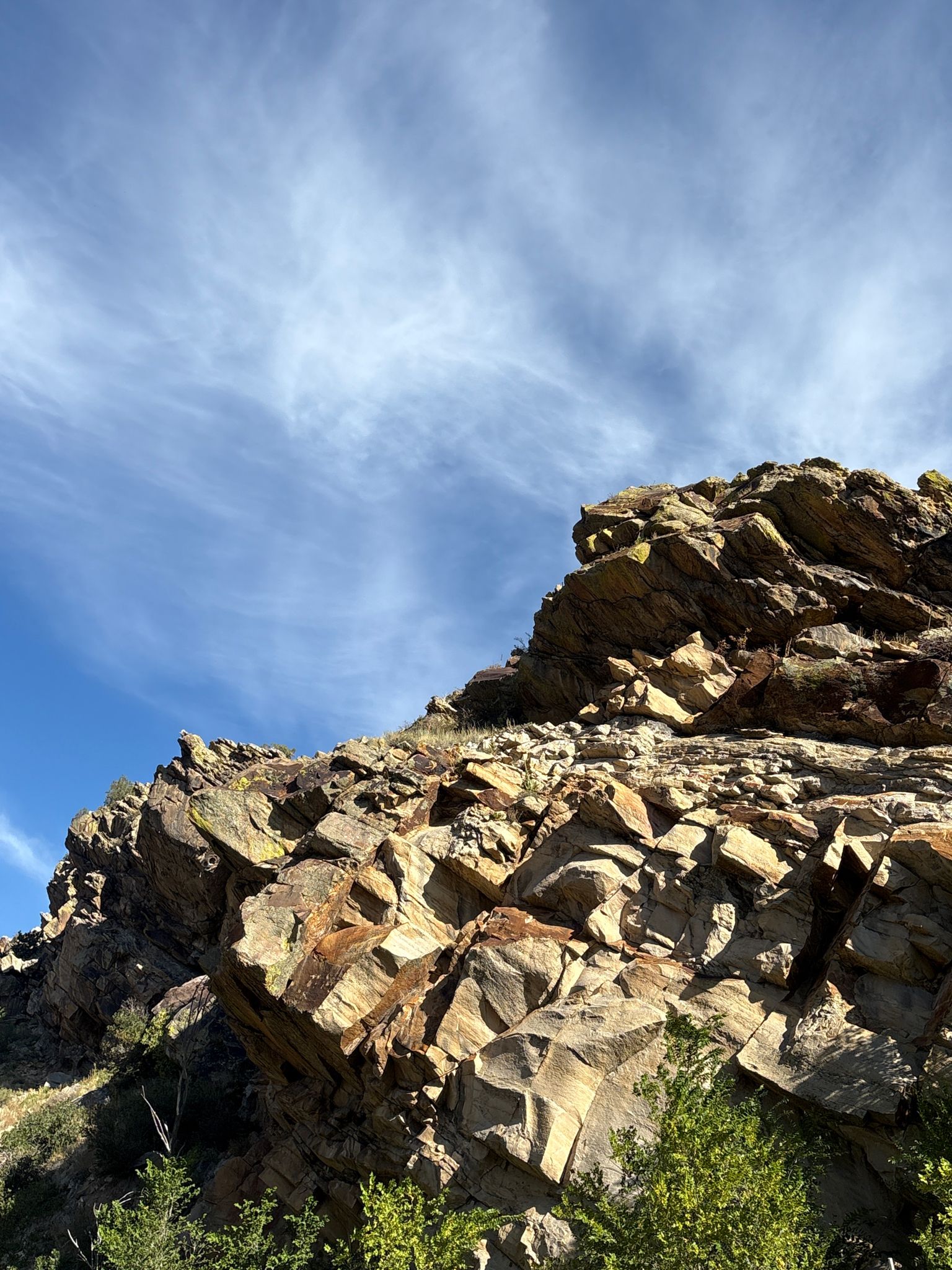 Jagged, layered rock formation under a bright blue sky with wispy clouds. - Bear Creek Trail