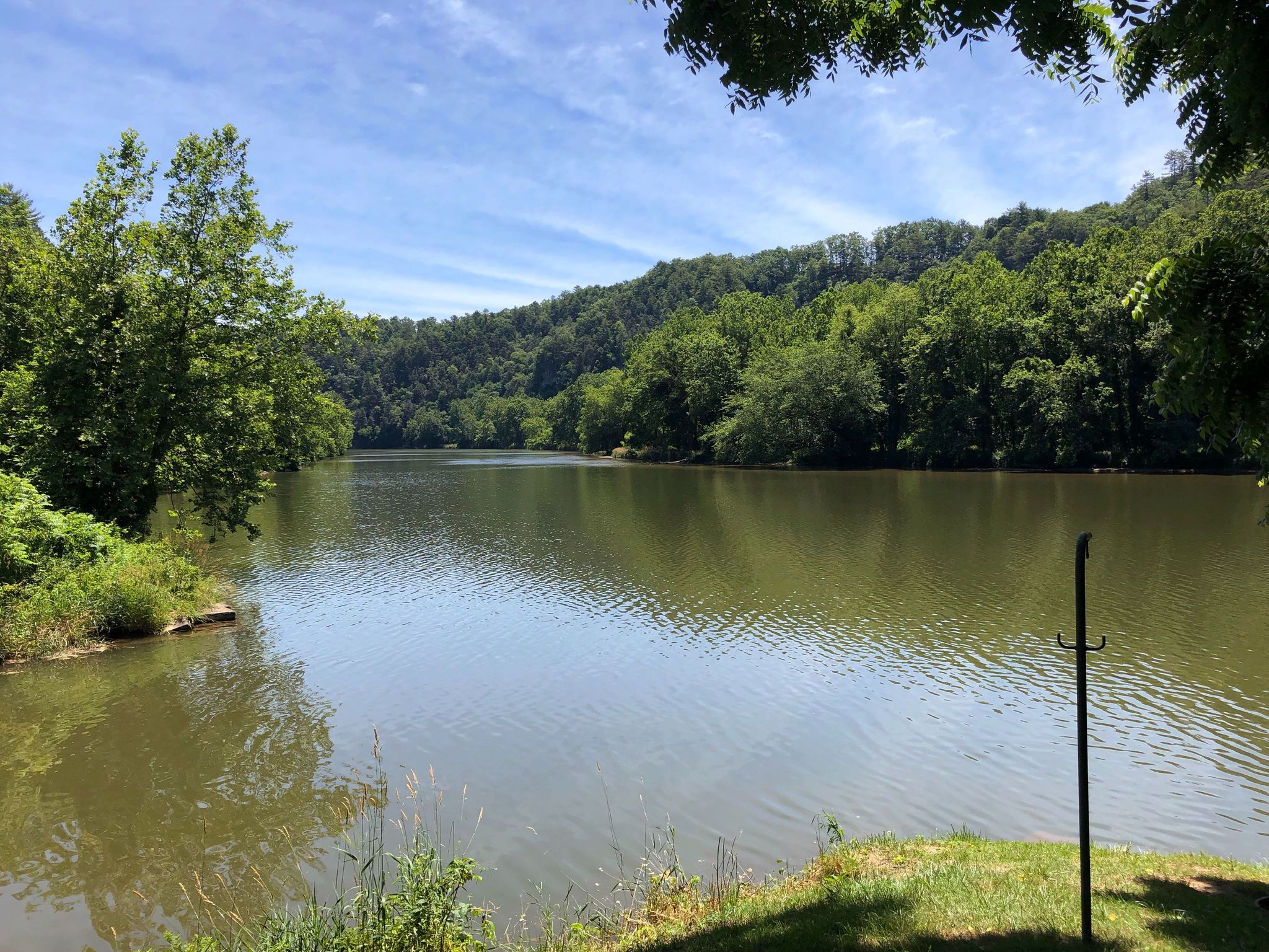 A wide, calm river with forested hills under a bright blue sky. - New River Trail