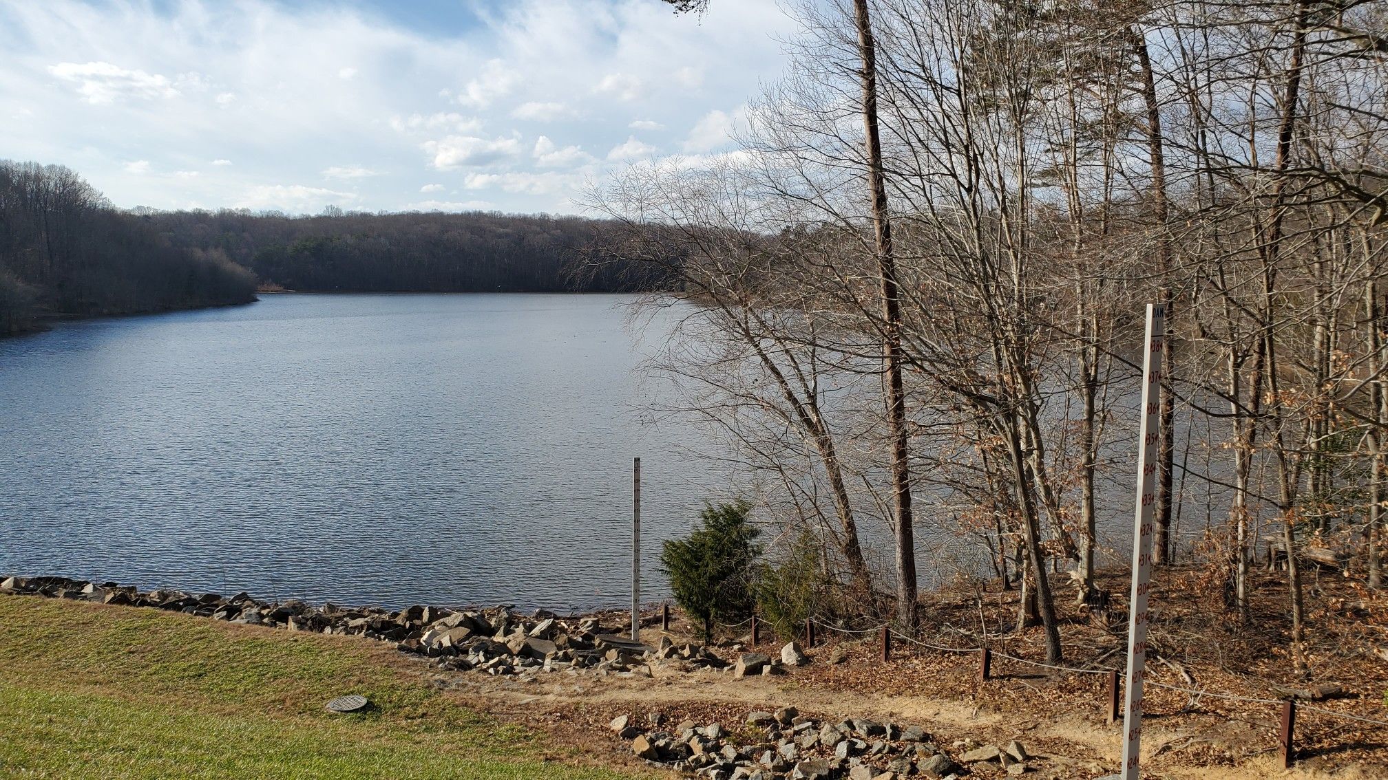 Lake with rocky shore, surrounded by bare trees under a cloudy sky. - Lake Mercer – Barrel Vault Bridge - Lorton loop from Newington Forest