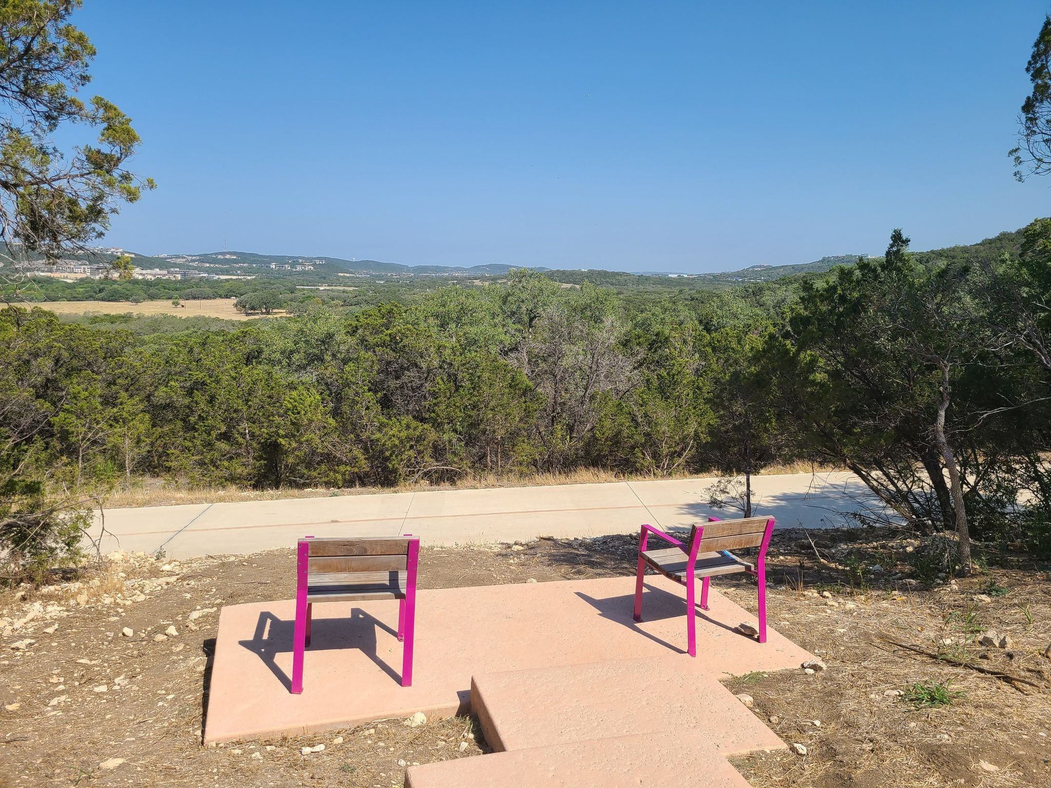 Two pink benches sit by a paved path, overlooking a wide green valley. - Salado Creek Trail – Morningstar Boardwalk loop from Six Flags Fiesta Texas