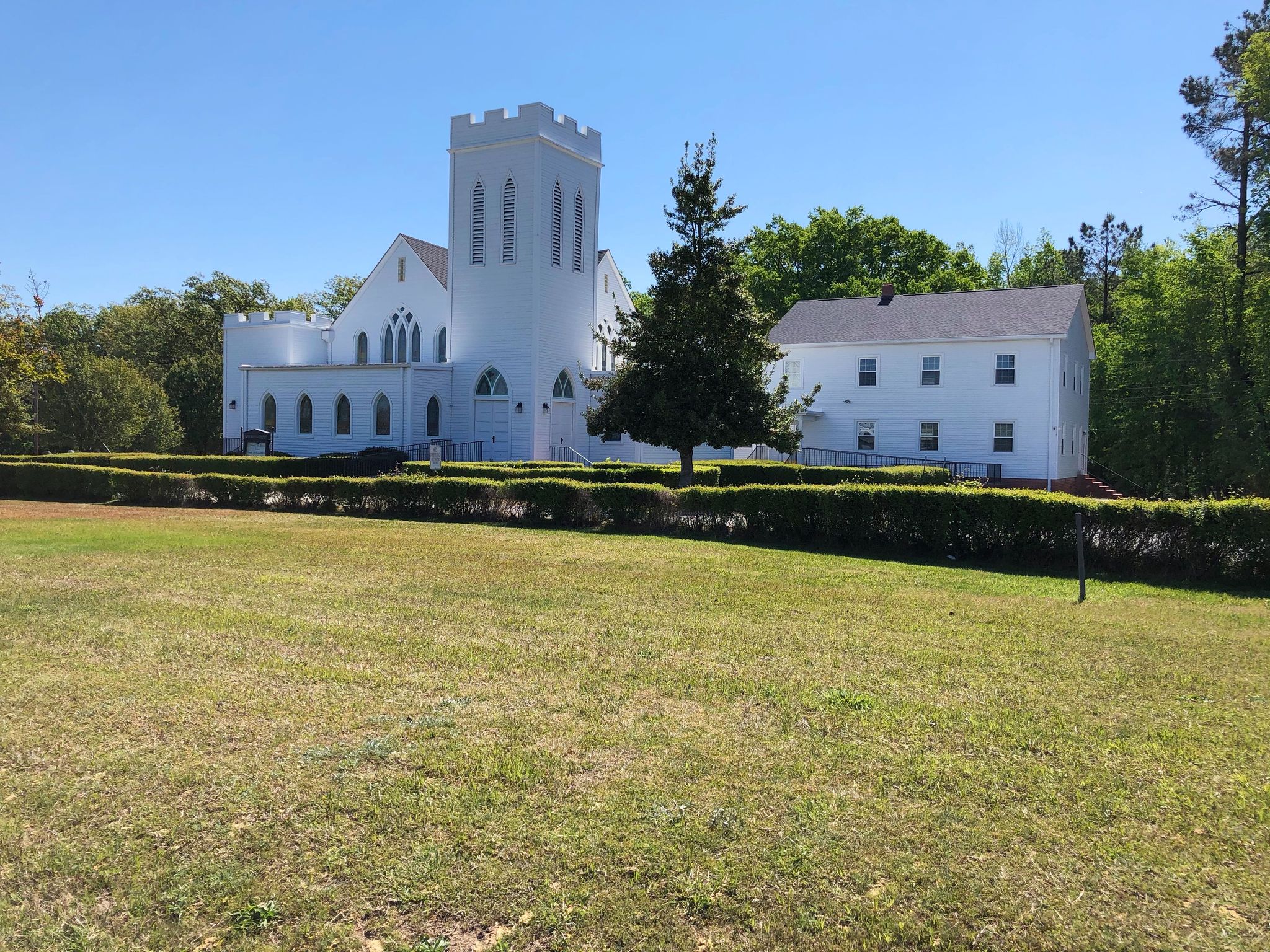 White church with a tall tower on a sunny day, surrounded by green grass and trees. - Ledge Creek Forest Conservation Area to John Hosea Kerr Reservoir loop