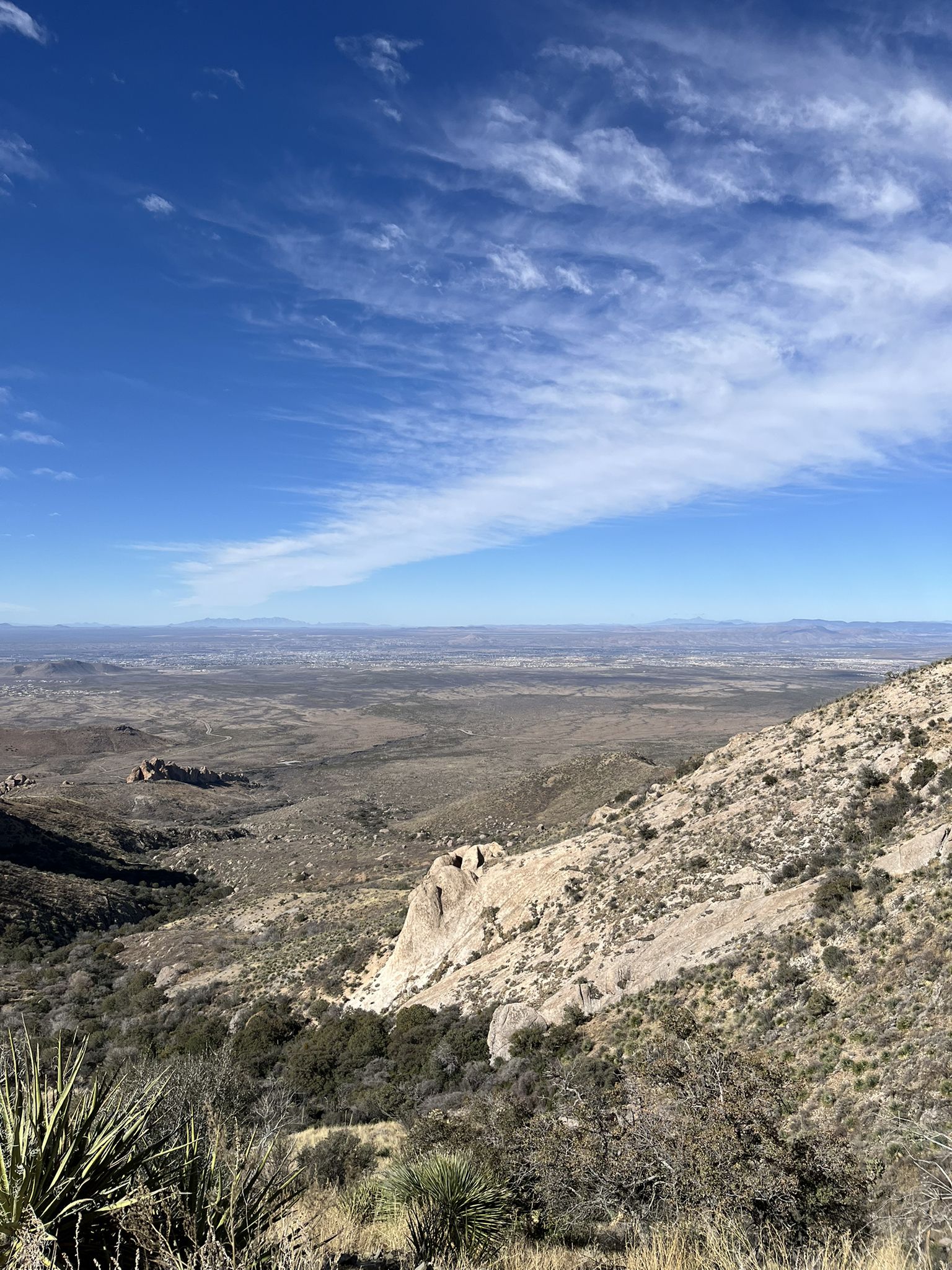 Vast desert landscape with distant mountains under a bright blue, cloudy sky. - Organ Needle from Baylor Canyon Road