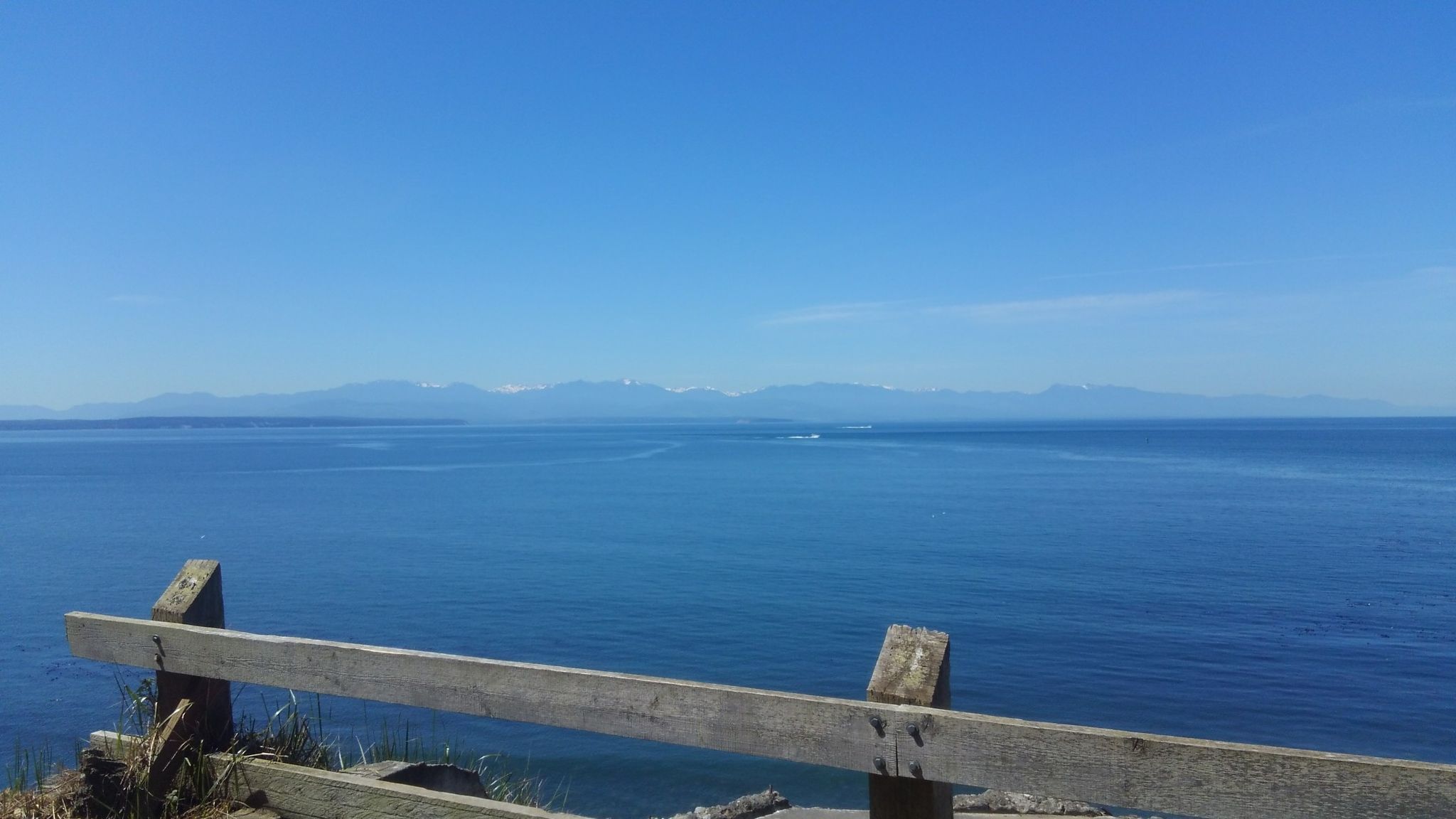 Wooden fence overlooking a vast blue ocean with distant mountains under clear sky. - Fort Ebey State Park loop from Fort Ebey State Park