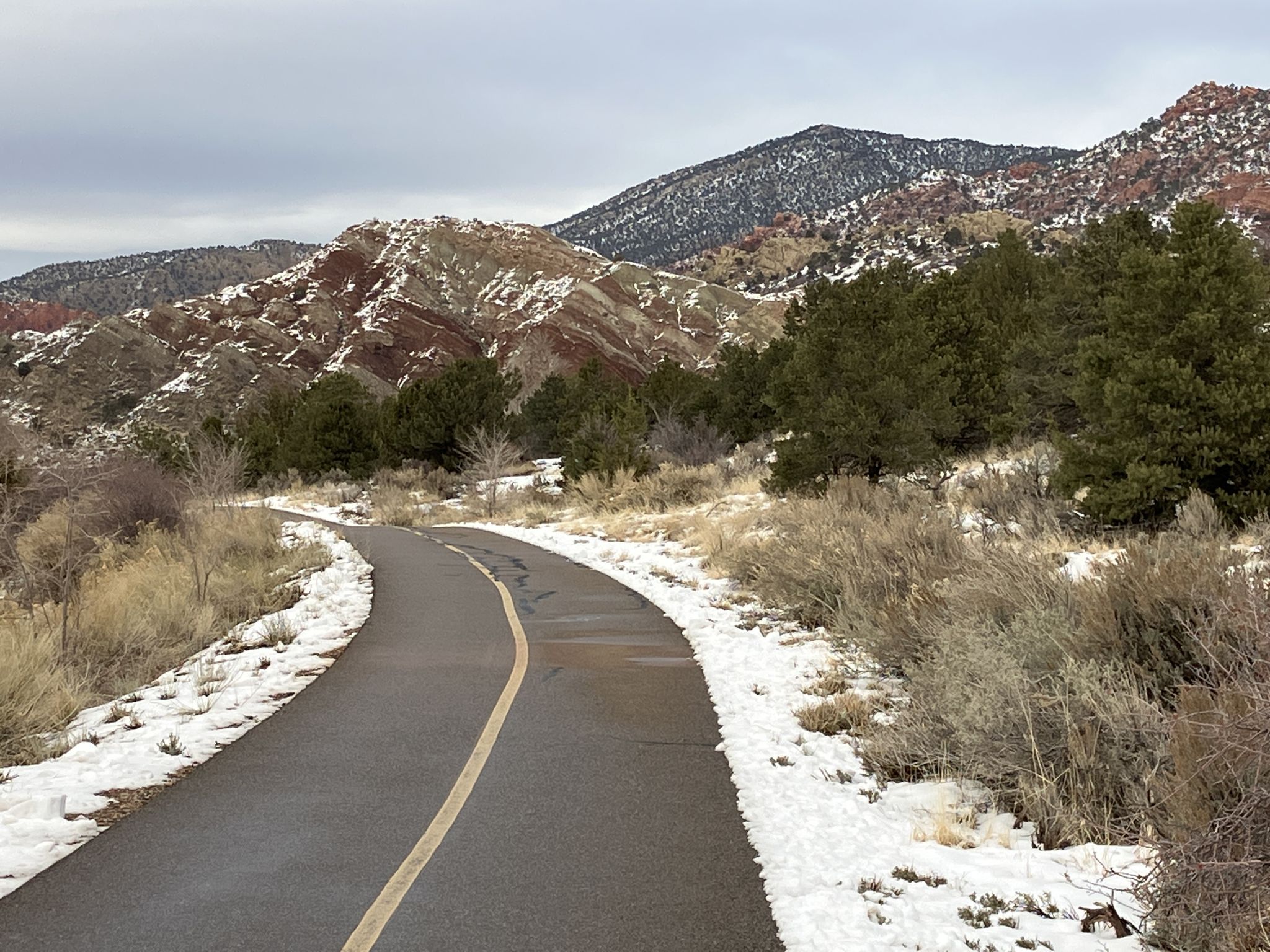 Paved path winding through snow-dusted mountains under an overcast sky. - Coal Creek Trail – East Bench Trail loop from Cedar City