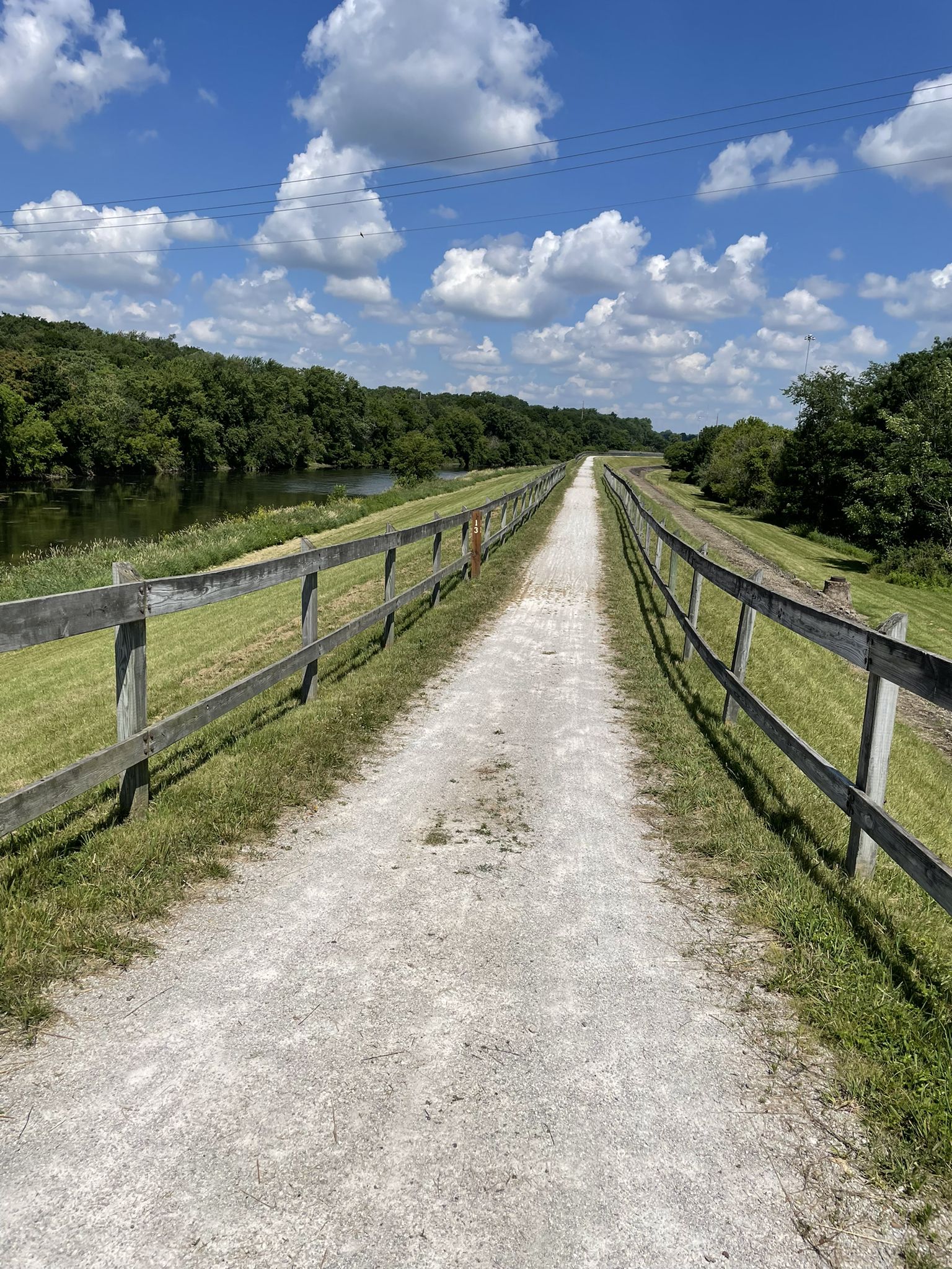Long gravel path with wooden fences beside a river under a sunny sky. - Ohio & Erie Canal Towpath Trail