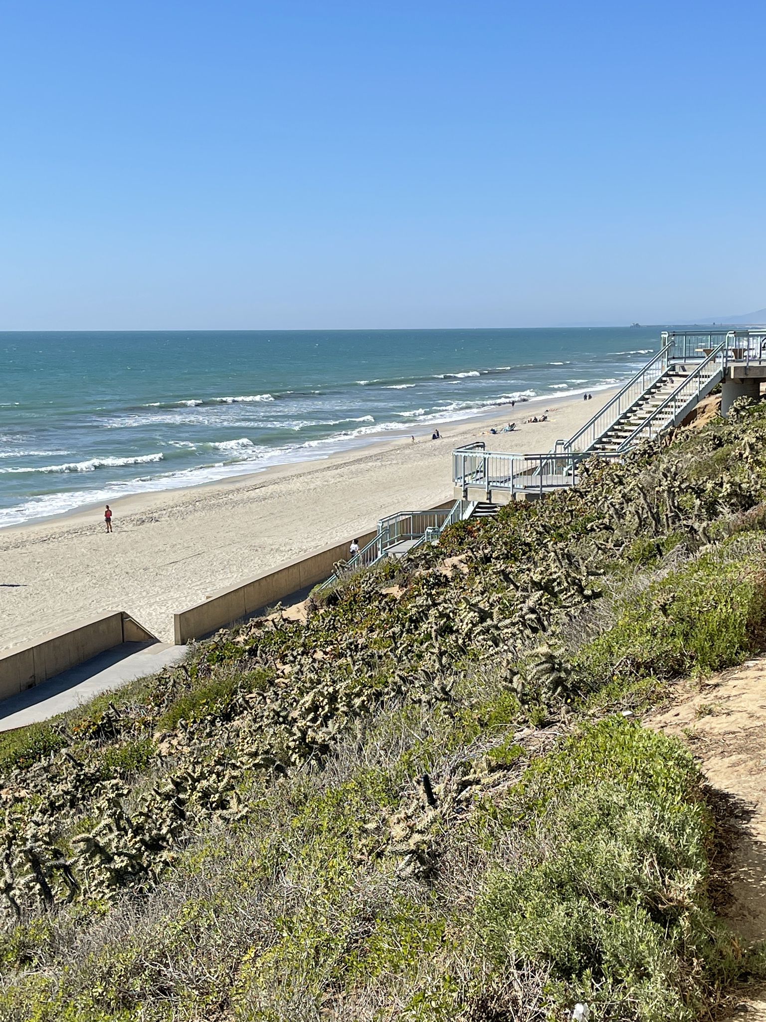 Sunny beach with ocean waves, sandy shore, and stairs descending from a green hillside. - Tamarack Beach – Tamarack Beach loop from Carlsbad