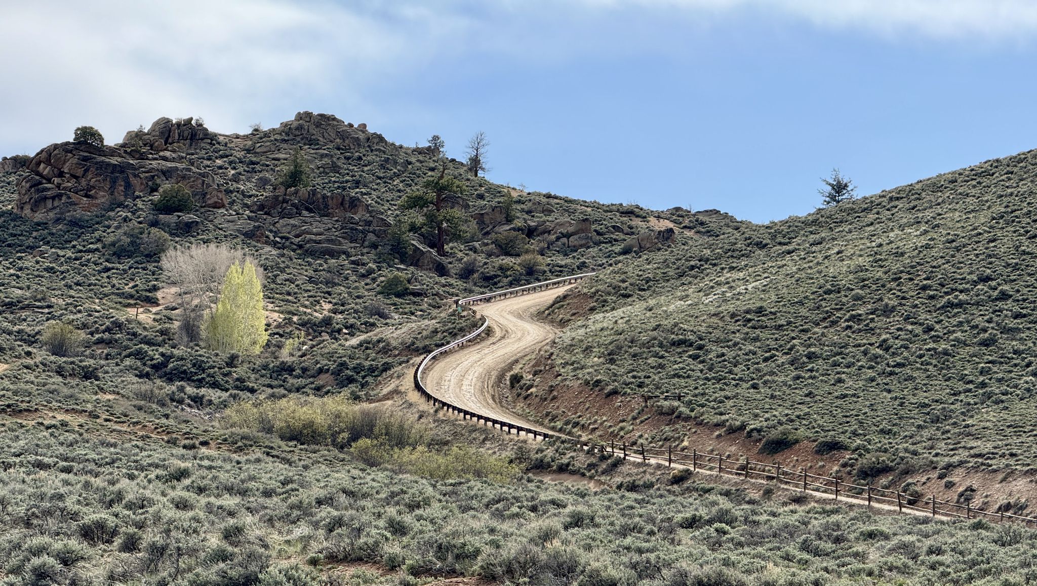 A winding dirt road ascends through arid, shrub-covered hills on a clear day. - Hartman Rocks Loop