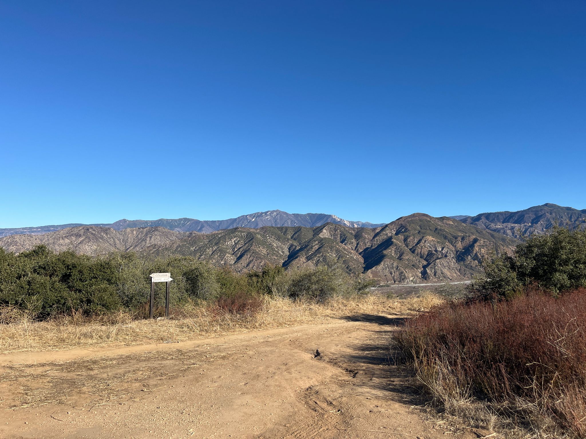 A dirt path leads towards distant rugged mountains under a clear blue sky. - Crafton Hills and Zanja Peak Loop