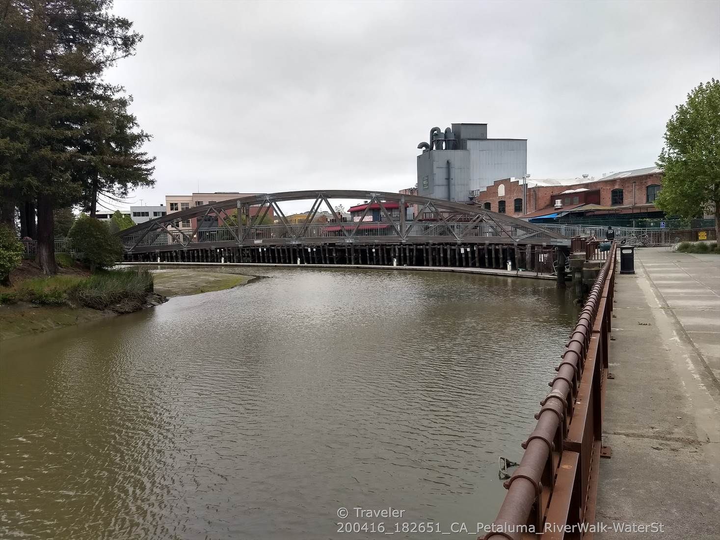 A river flows past an old wooden bridge and industrial buildings on a cloudy day. - Bay Area Ridge Trail: Lynch Creek Trail
