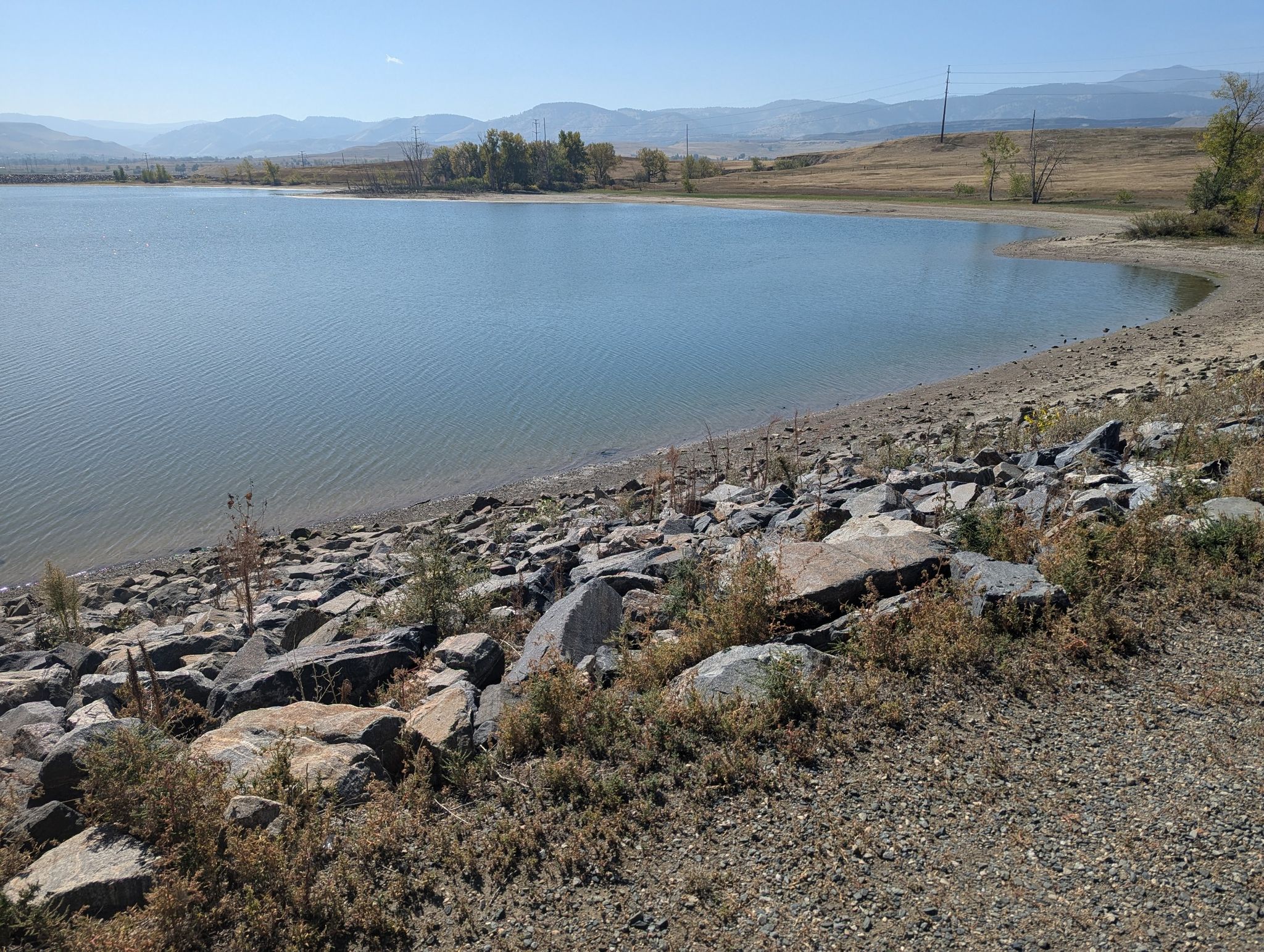 Sunny view of a lake with a rocky shore and distant mountains. - Tucker Lake Trail