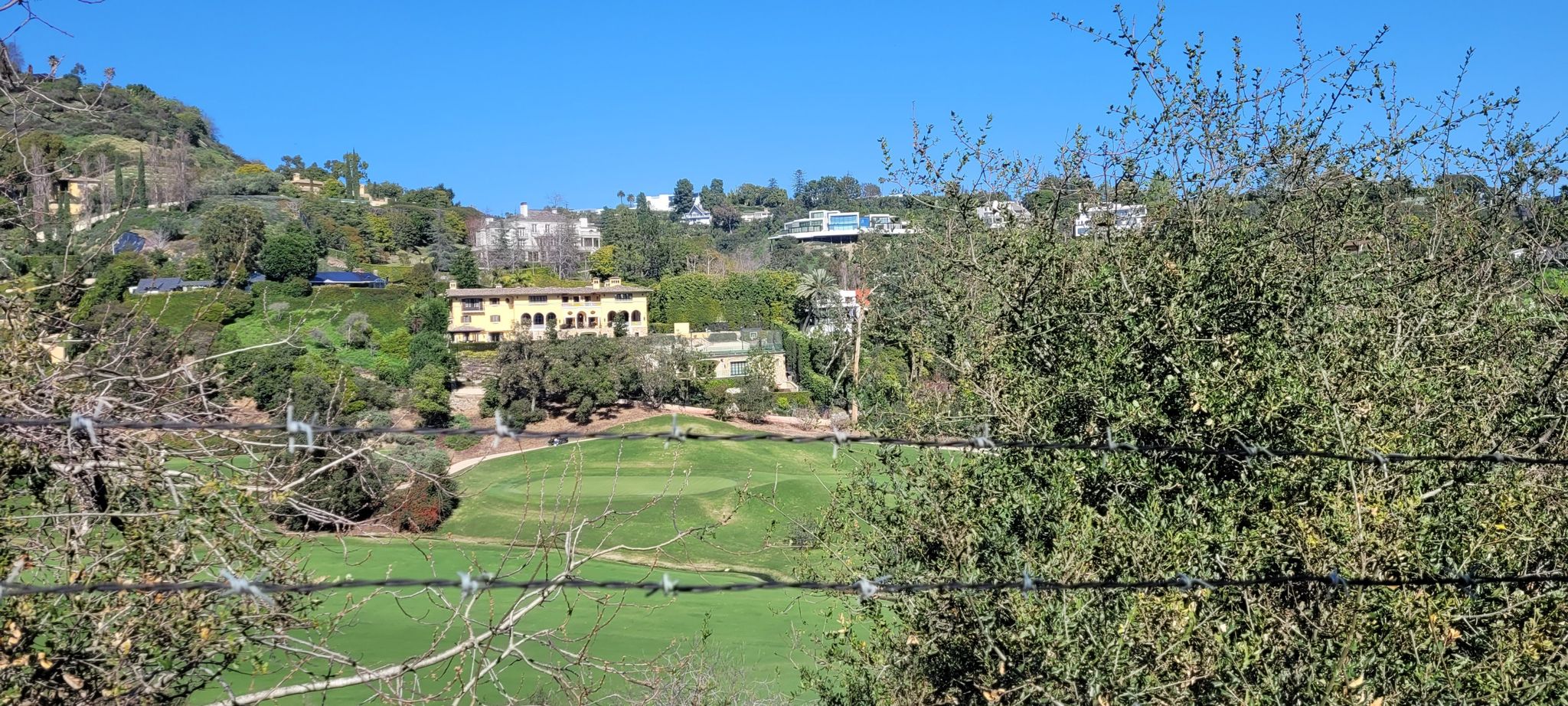 A green golf course nestled in a valley with houses on surrounding hills. - Little Tujunga Canyon Loop