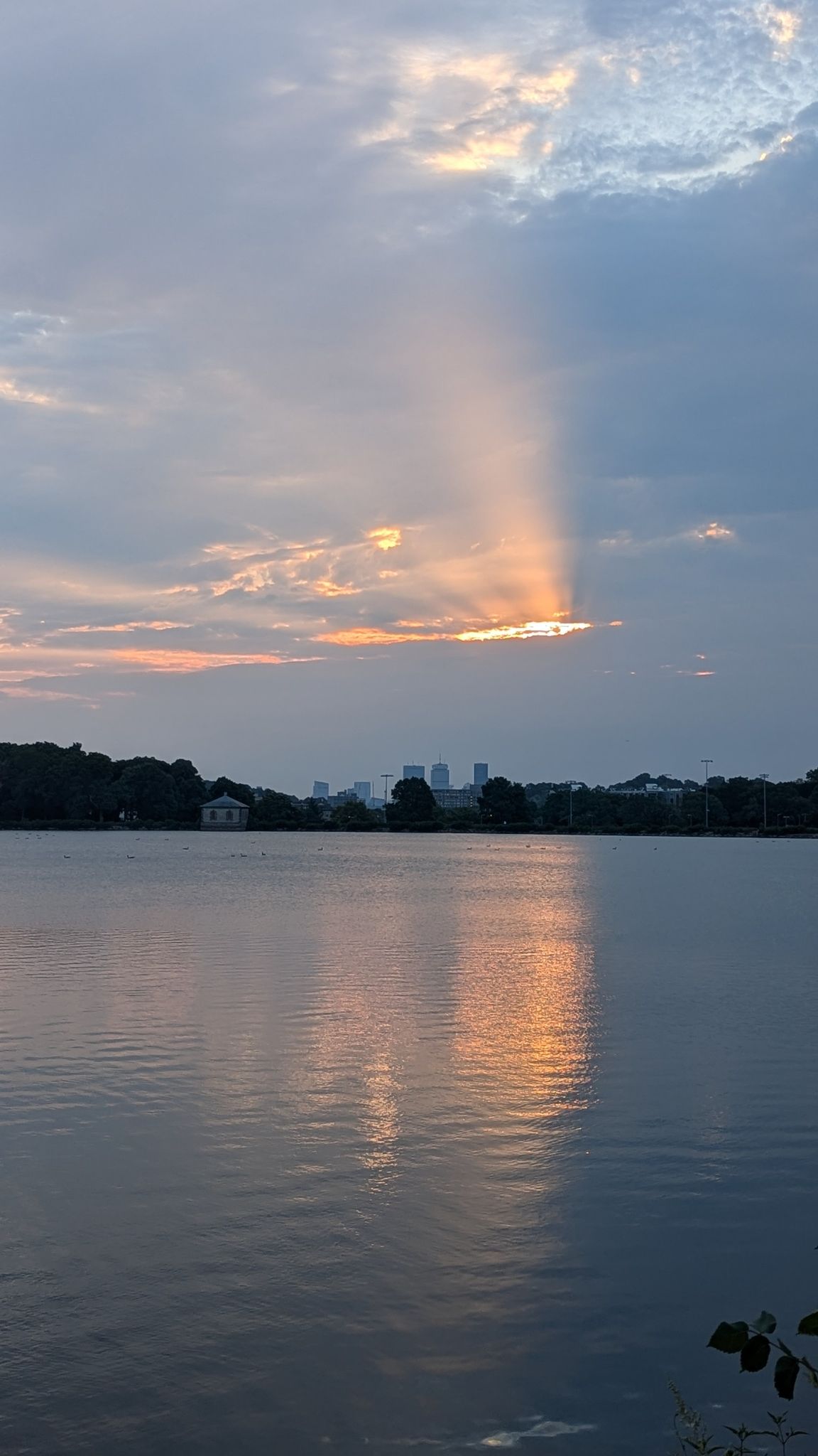 Sunset over a calm lake with crepuscular rays and distant city silhouette. - Boston Marathon Training Loop