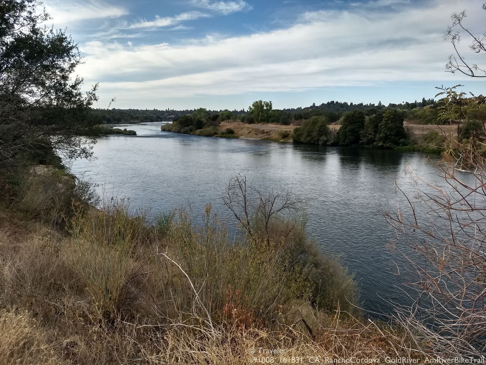 Wide river flowing under a cloudy sky, flanked by green and brown vegetation. - Hiking loop from Fair Oaks