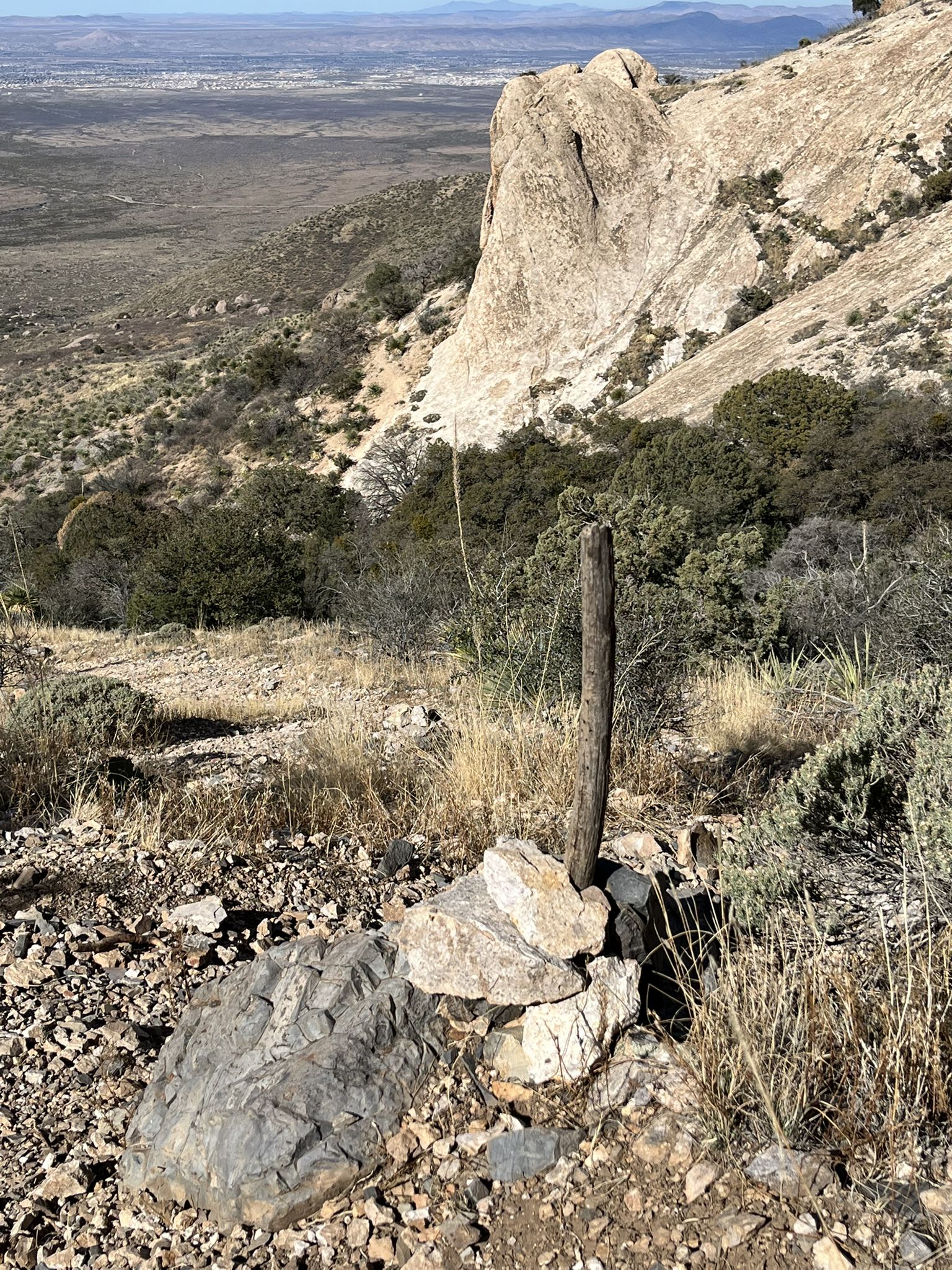 Wooden post marker on a rocky hillside overlooking a vast, arid valley. - Organ Needle from Baylor Canyon Road