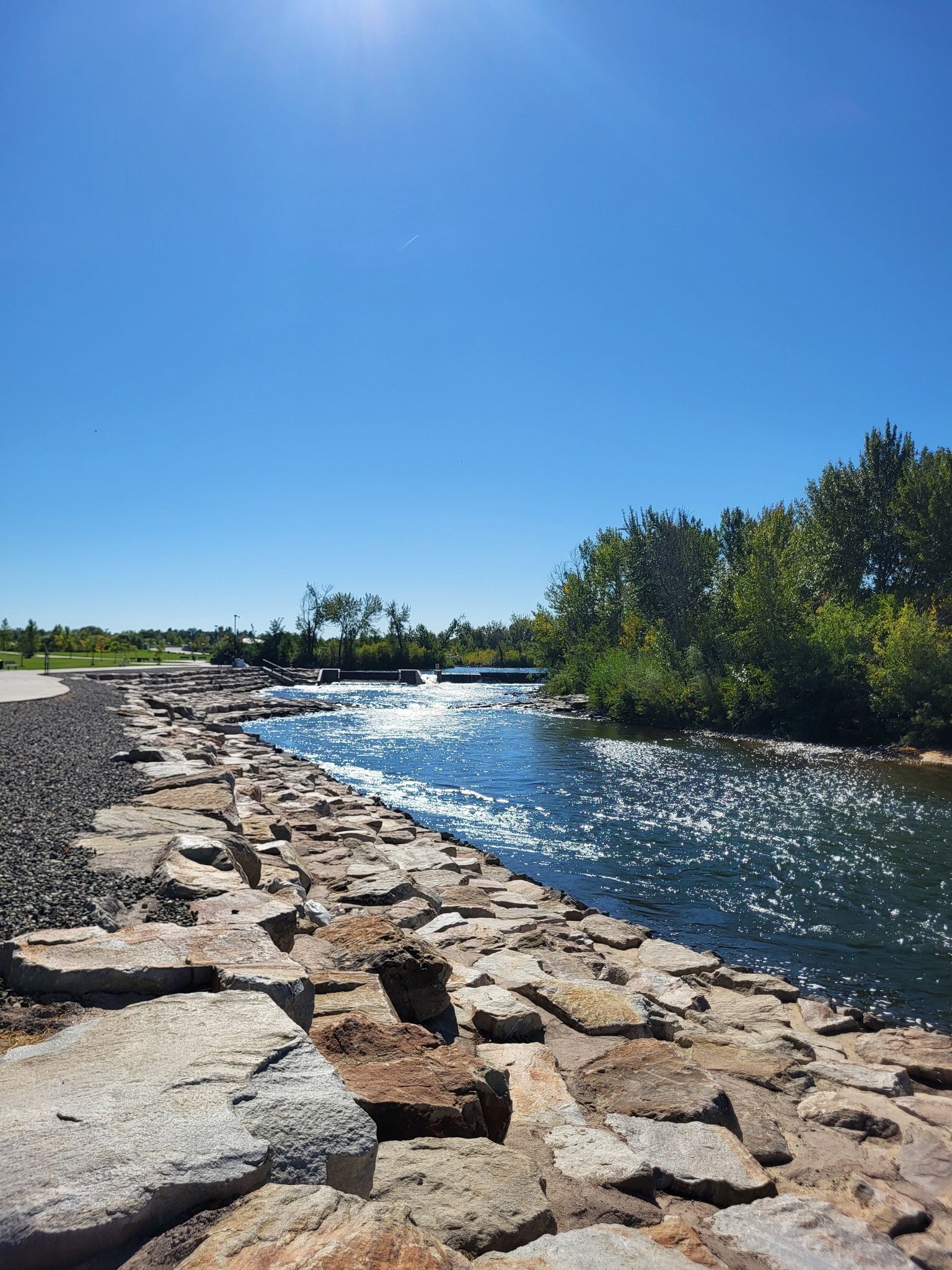 Bright sunny day over a river with a rocky bank and green trees. - Boise River Greenbelt – Boise River Greenbelt loop from Military Reserve