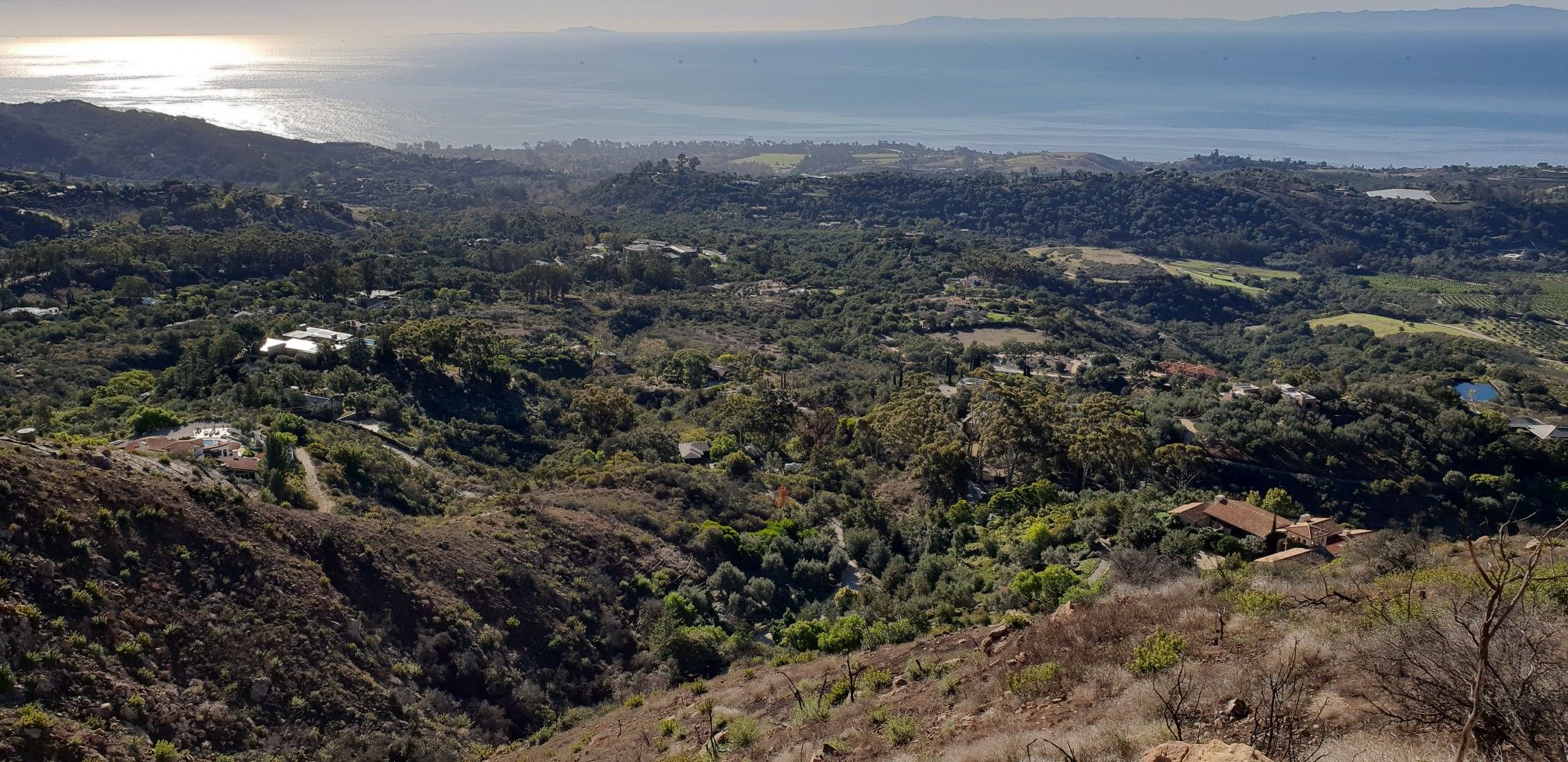 Expansive view of green hills, ocean, and scattered buildings under bright sun. - Romero Canyon Trail Loop