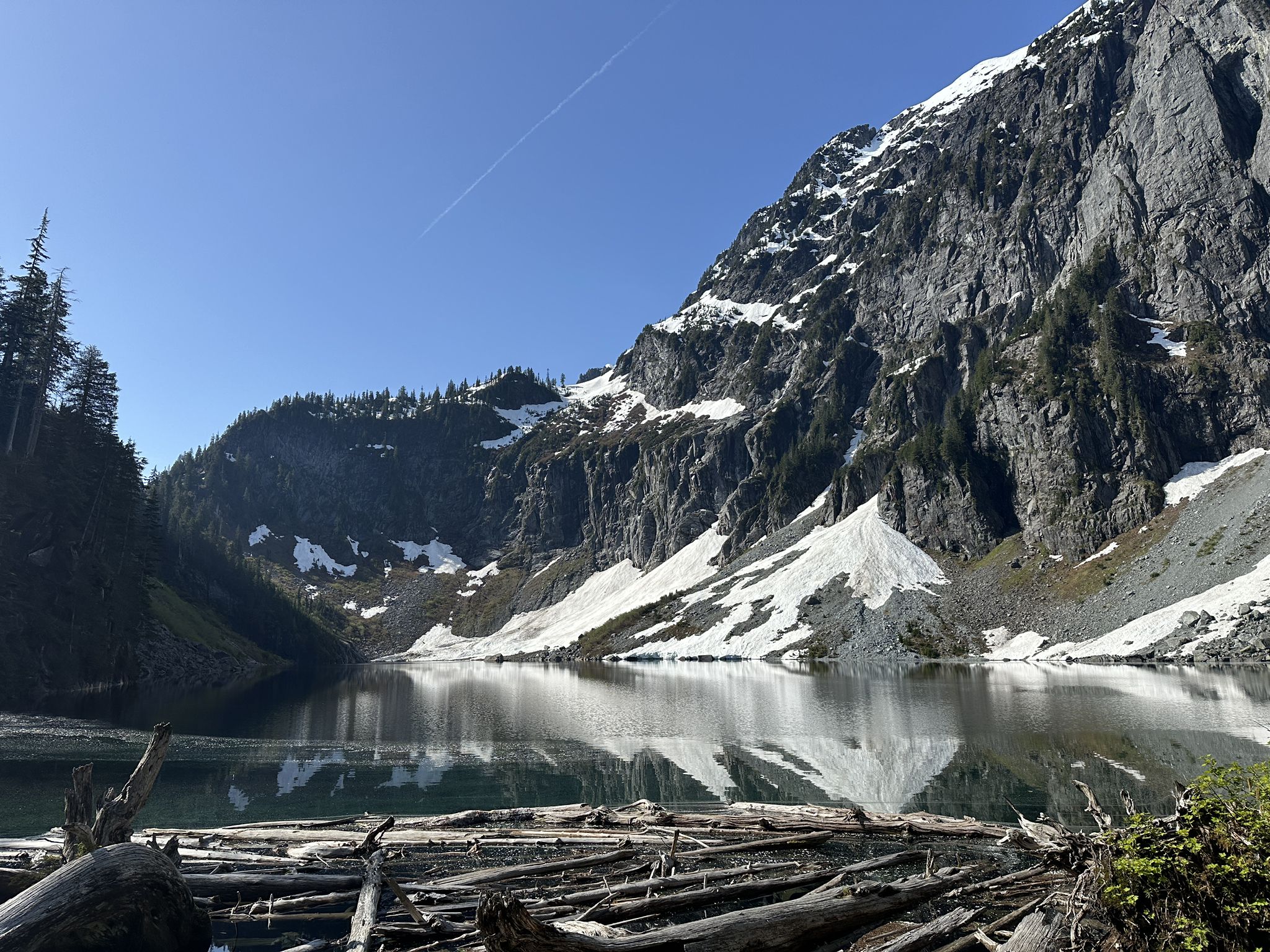 Calm mountain lake reflecting snow-capped peaks and blue sky, with driftwood. - Lake Serene and Bridal Veil Falls Trail