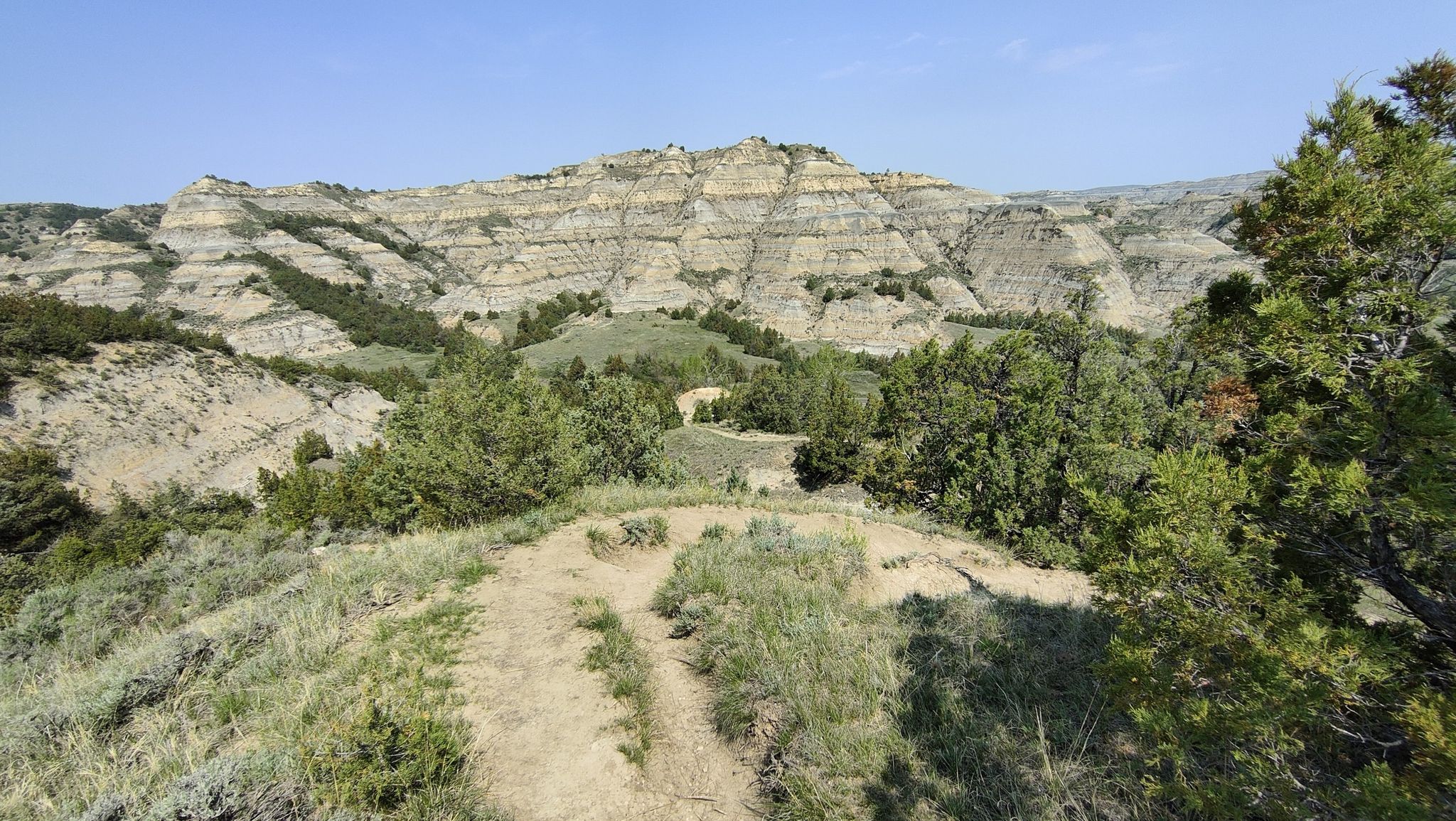 Dirt path overlooking distant layered rock formations and green valleys. - Hiking loop from Riverbend Overlook