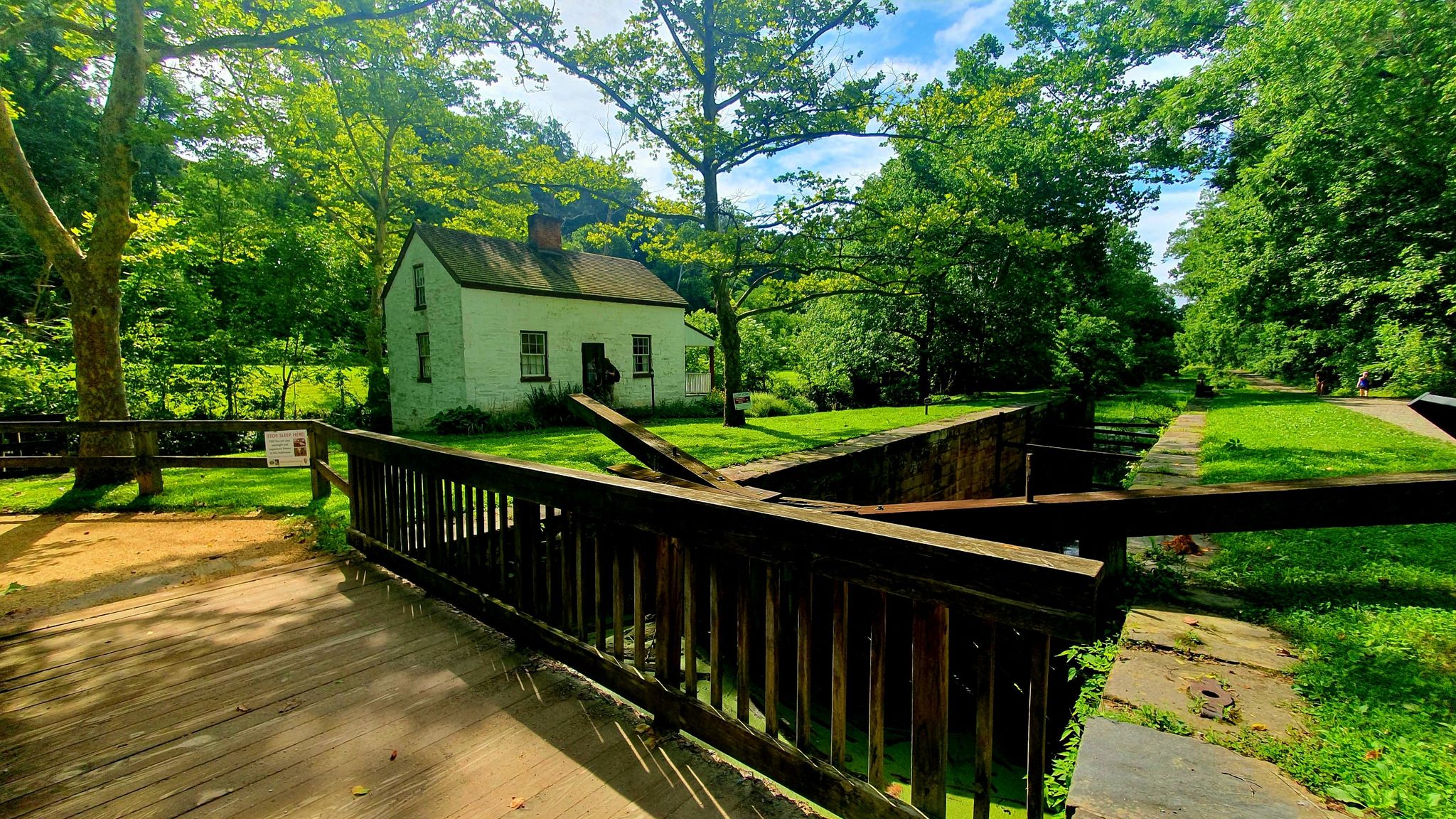 Historic white house next to a wooden bridge and canal lock on a sunny day. - Capital Crescent and Little Falls Trail Loop