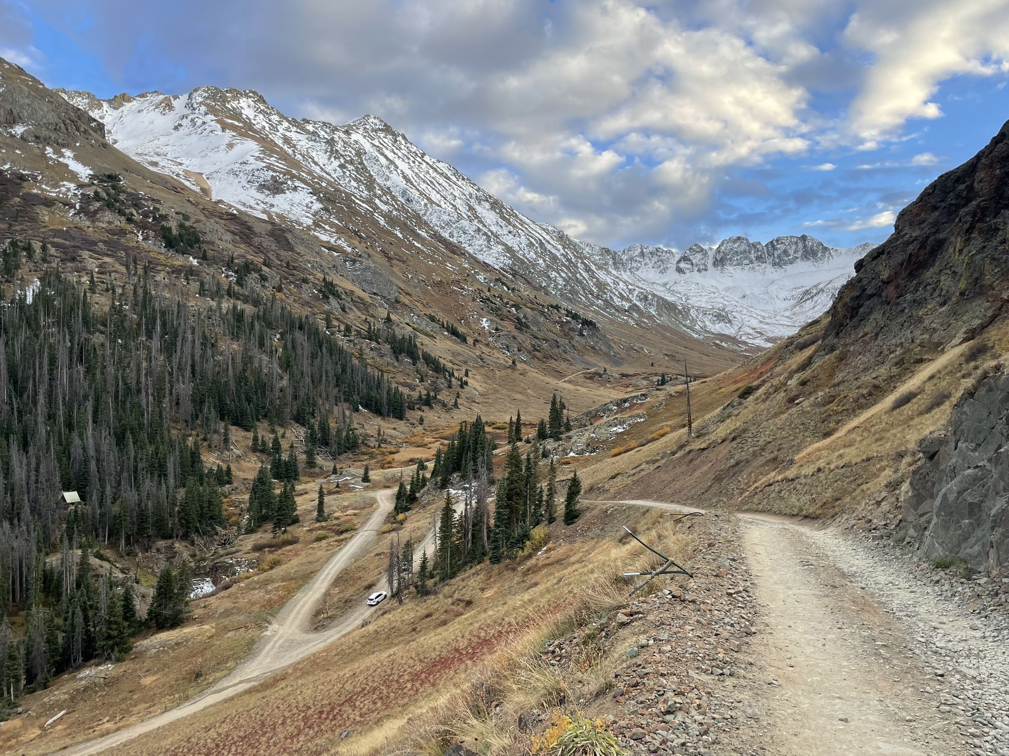 Dirt road winding through a mountain valley with snow-capped peaks and pine trees. - Cinnamon Pass from Cataract Gulch Trailhead