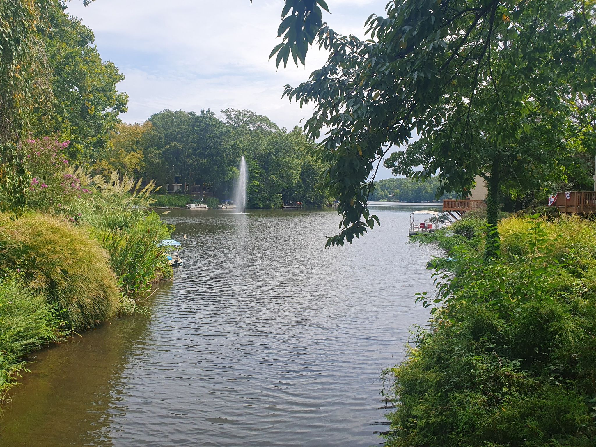 A narrow waterway with a distant fountain, surrounded by dense green trees. - Lake Anne Village Center loop from Reston