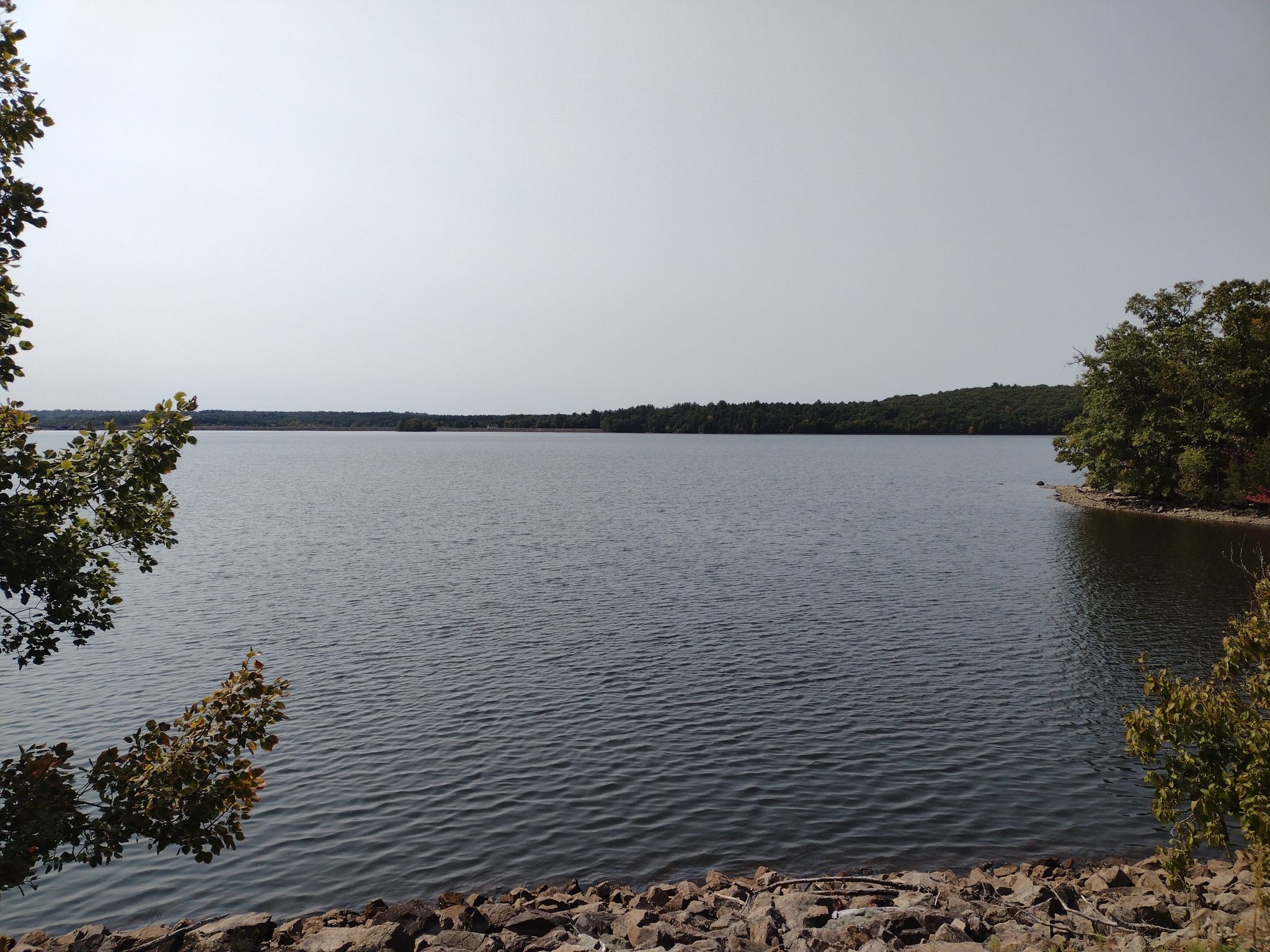 A wide lake with a rocky shore and distant forested banks under a bright sky. - High Street loop from North Attleborough