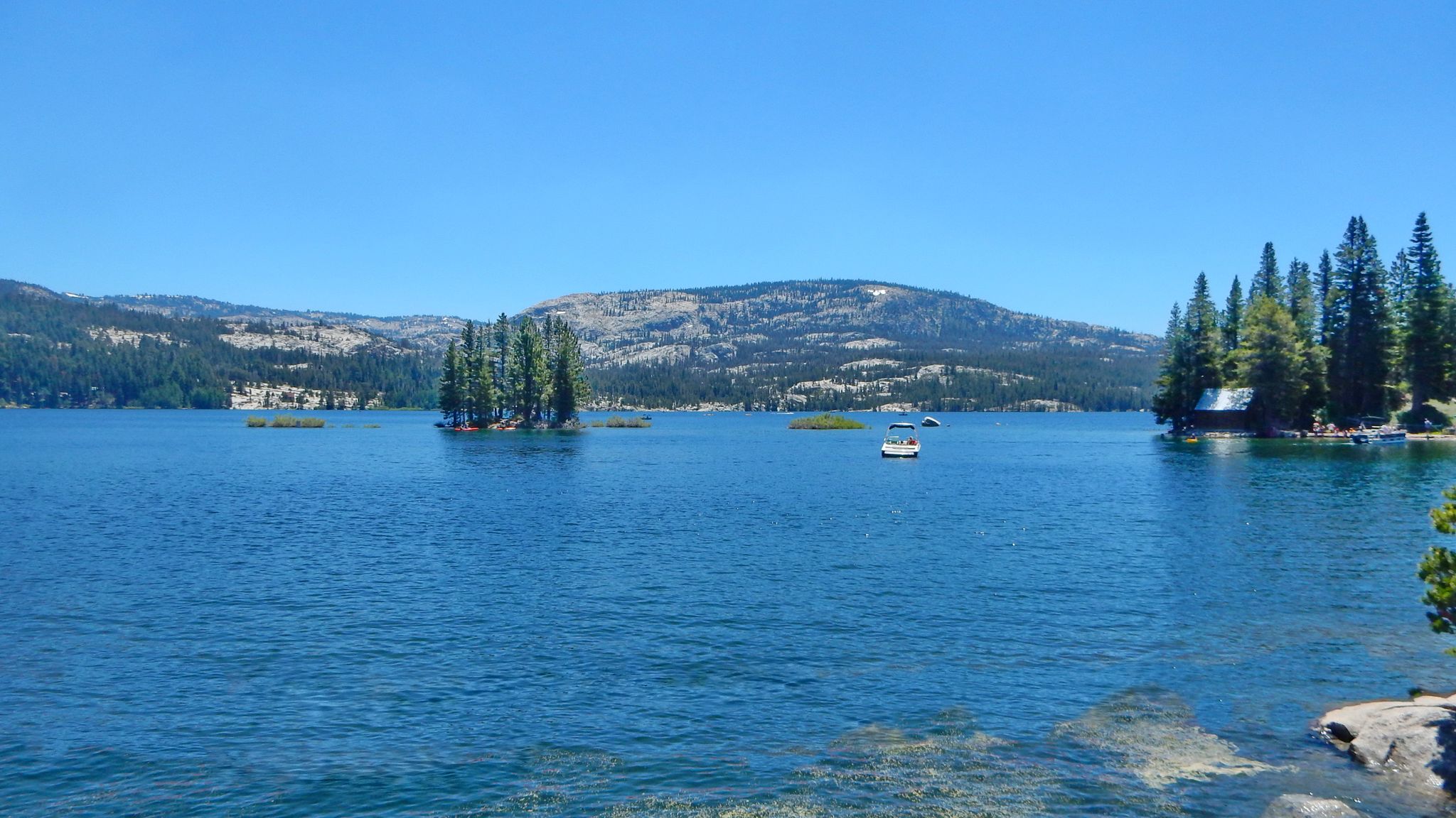 A wide blue lake with forested islands and a small boat under a sunny sky. - Silver Lake via CA 88