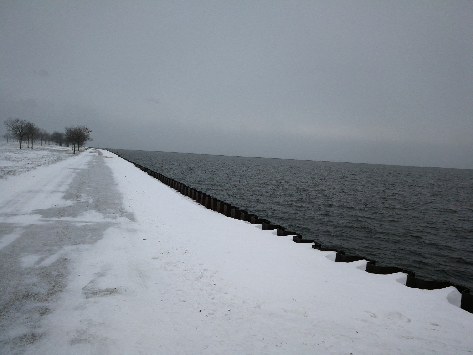 Snow-covered path next to dark water under an overcast winter sky. - Oak Leaf Trail: Milwaukee River and Lake Loop