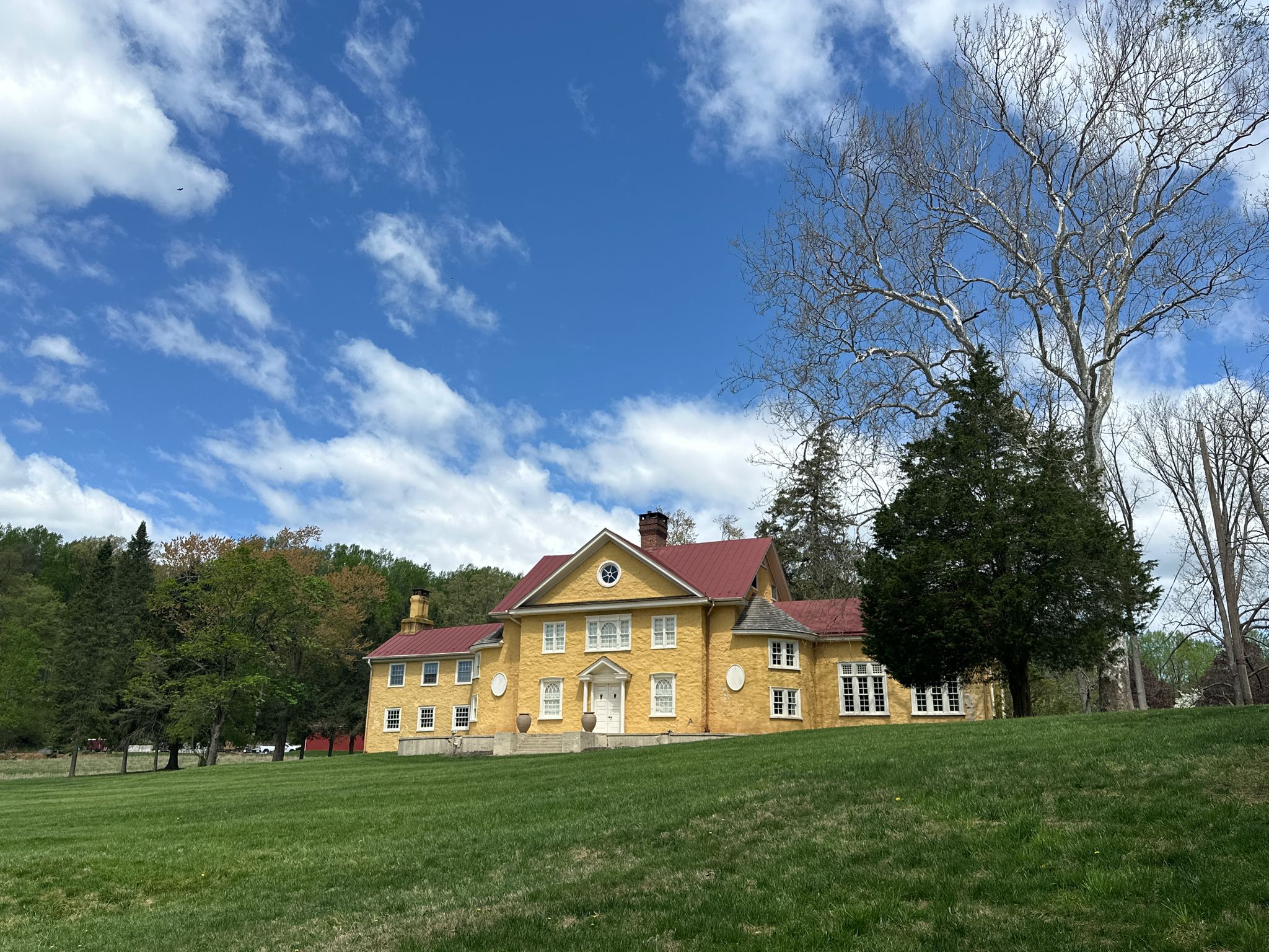 Large yellow house with red roof on a sunny day, surrounded by trees. - Forest Hill, Forge, Lake, and Cedar Hollow Trails Loop