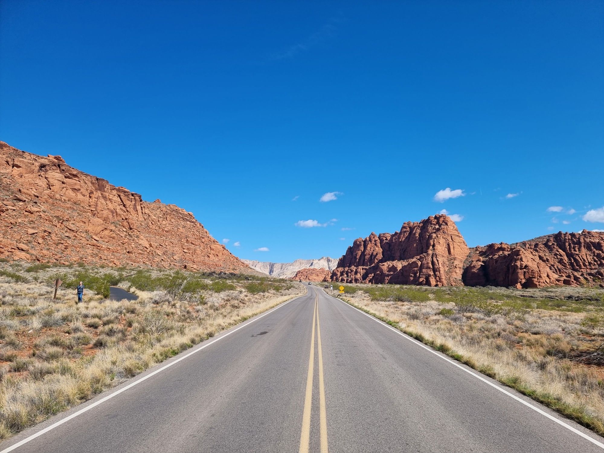 A straight desert road extends between towering red rock cliffs under a clear sky. - Snow Canyon State Park loop