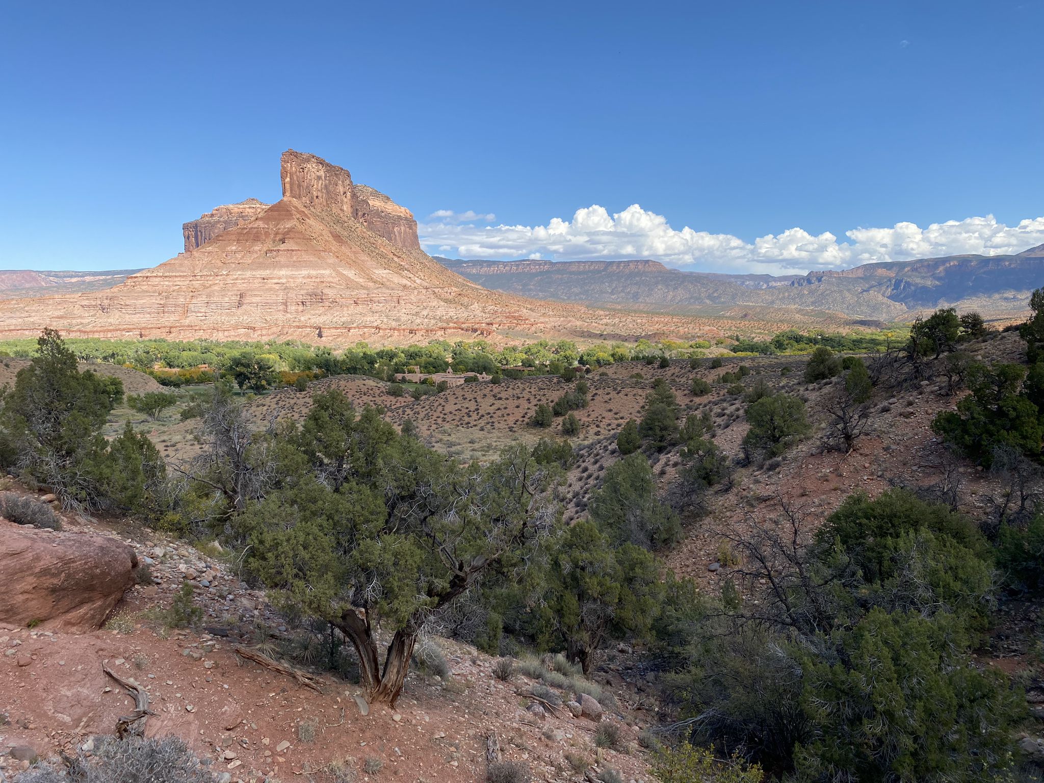 Panoramic view of a red mesa overlooking a green valley and desert hills. - Hiking loop from Cantina Pool Bar & Grill