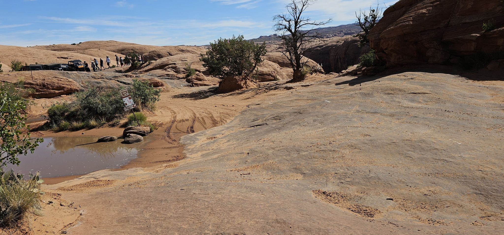 Rocky desert terrain with a muddy puddle and a group of people. - Hell's Revenge 4x4 Trail