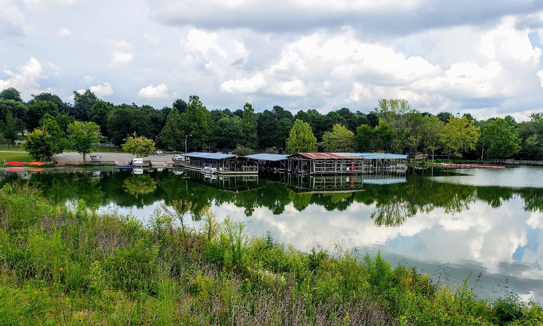 Boat docks on a calm lake surrounded by green trees under a cloudy sky. - Lake Fayetteville Trail – Boardwalk along Spring Creek loop from Johnson