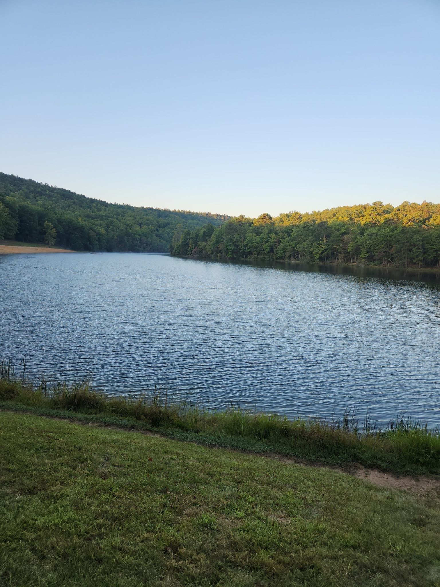 Serene lake surrounded by green, tree-covered hills under a clear sky. - Indian Creek and Moore's Wall Loop Trail