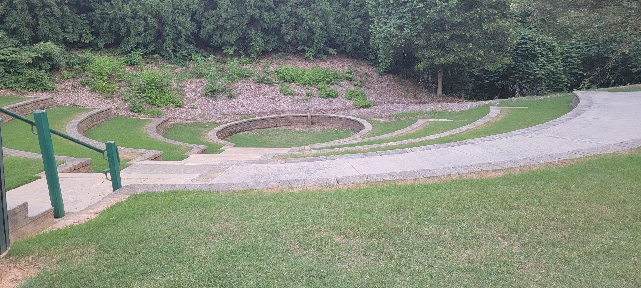 Empty outdoor amphitheater with terraced grass seating and concrete paths. - Rock Creek Greenway