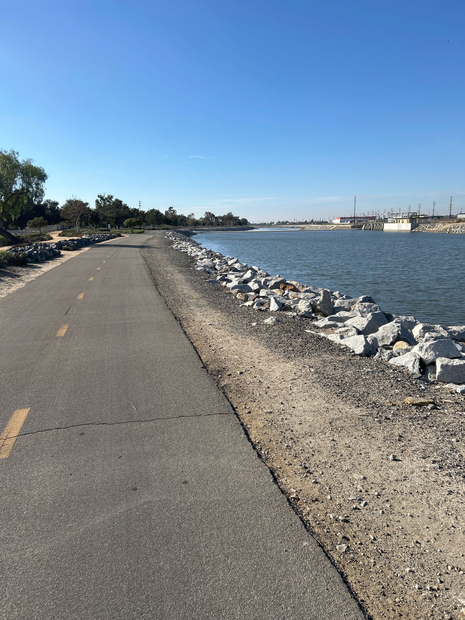 Paved path alongside a calm waterway on a bright sunny day. - Santa Ana River Trail