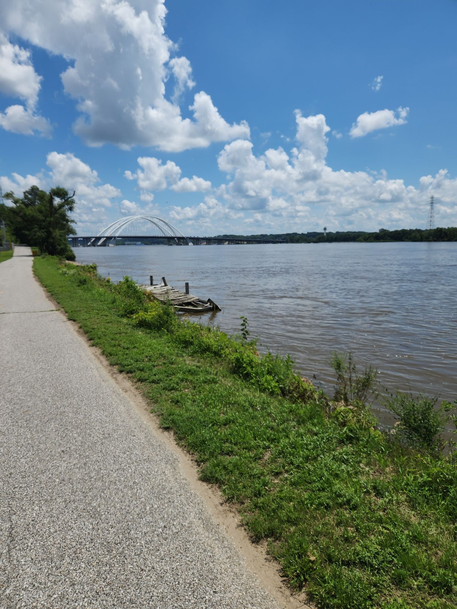 Paved path next to a wide river with a distant bridge on a sunny day. - Duck Creek Trail – Vander Veer Botanical Park loop from Davenport