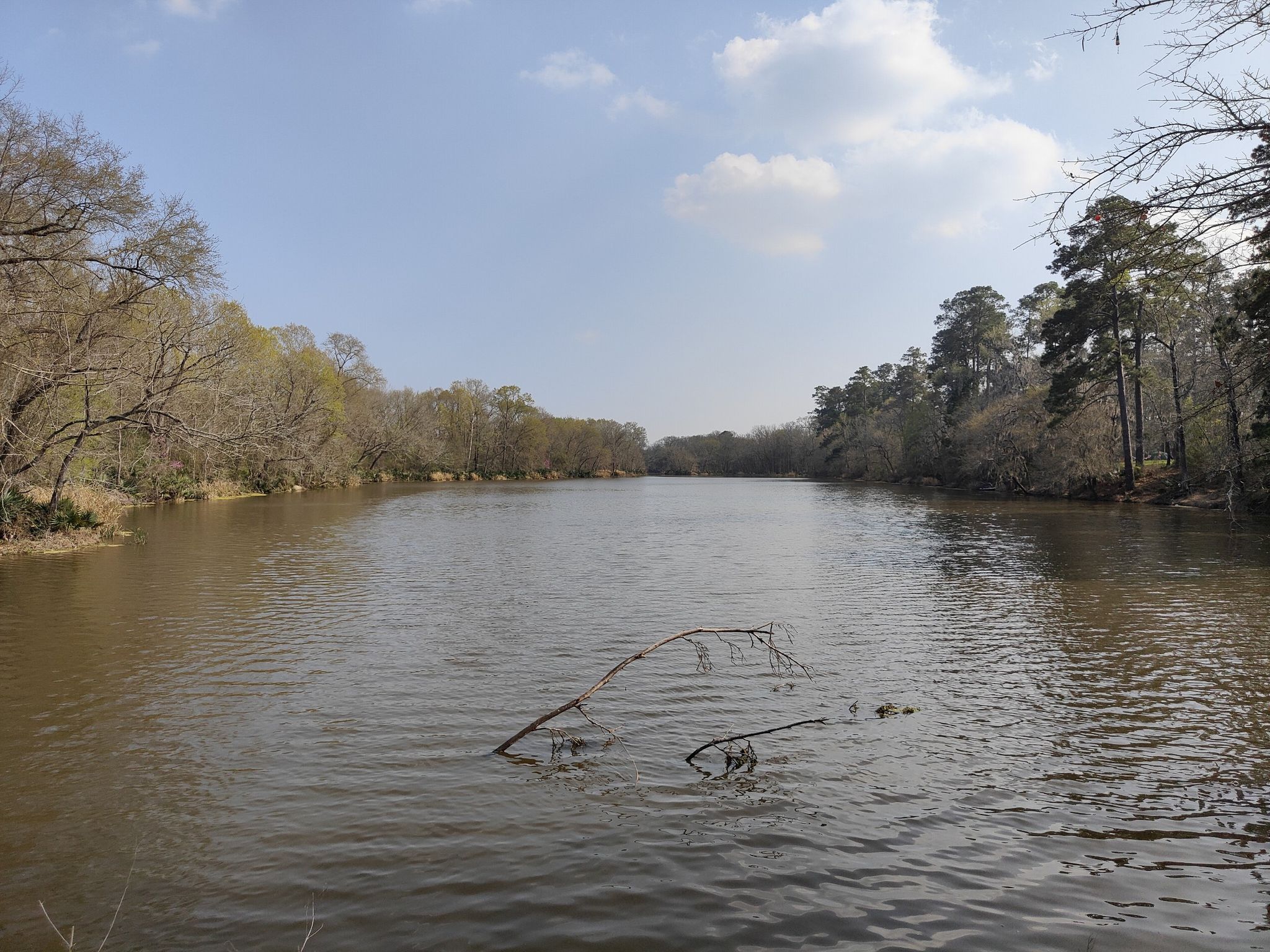 Wide river flowing between tree-lined banks under a partly cloudy sky. - Lake Conroe north loop